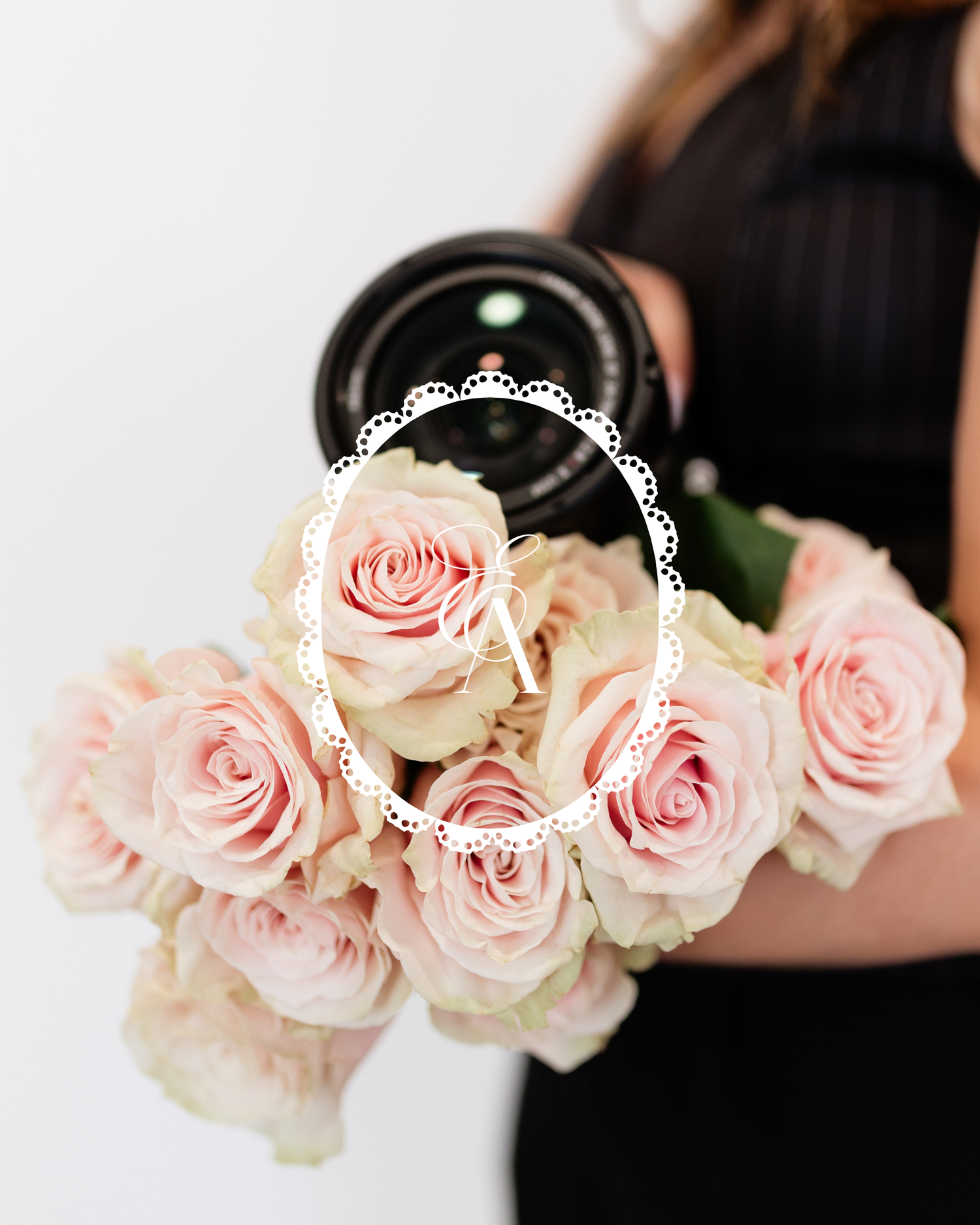 Woman in black dress holding a camera and bouquet of soft pink roses with a decorative white lace oval overlay.