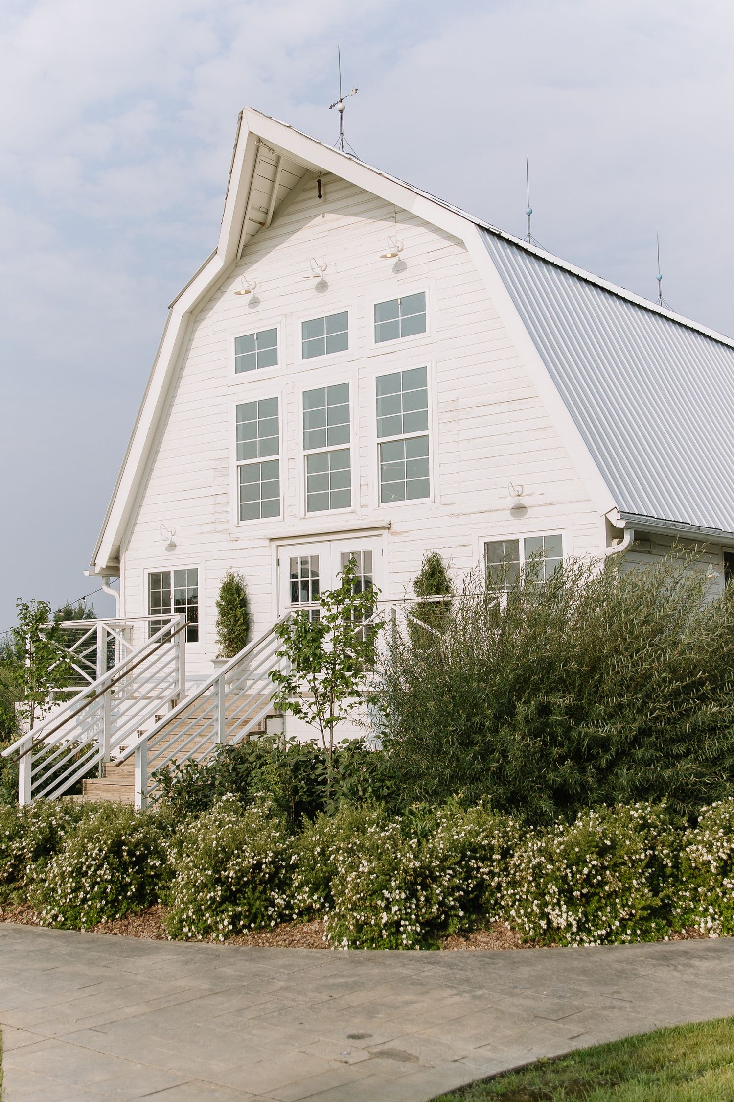 White barn wedding venue with gambrel roof, large windows, and manicured landscaping.