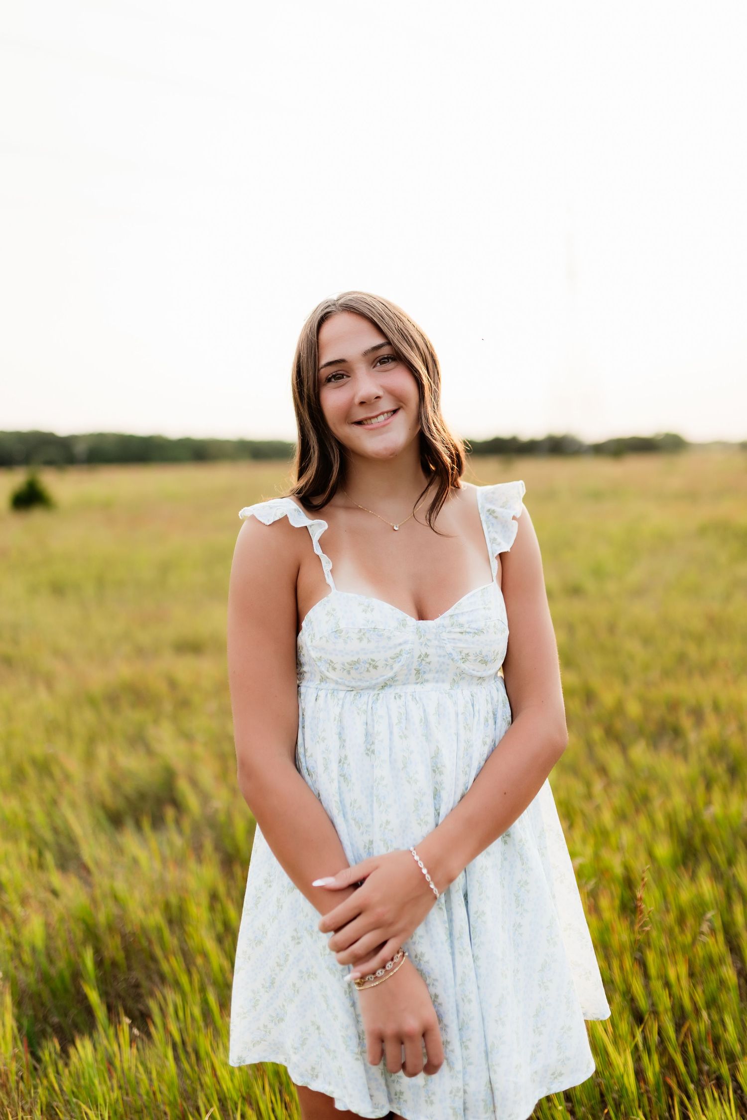 Teenage girl in light blue floral sundress standing in a golden grass field at sunset.