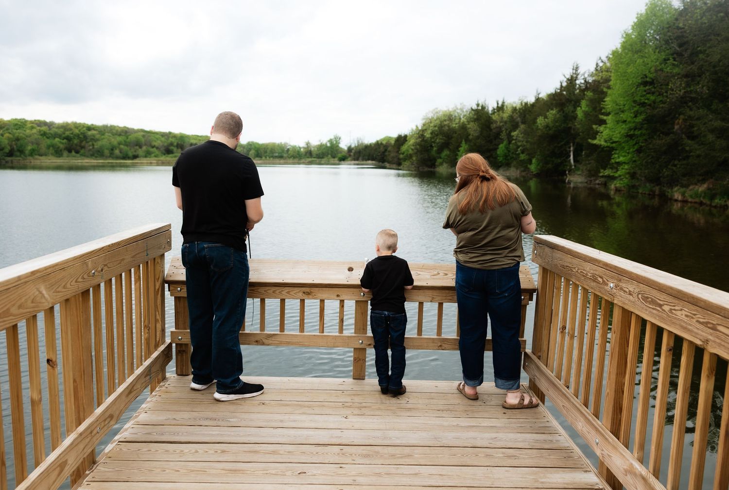 Family of three standing on a wooden dock fishing and enjoying a peaceful lake view.