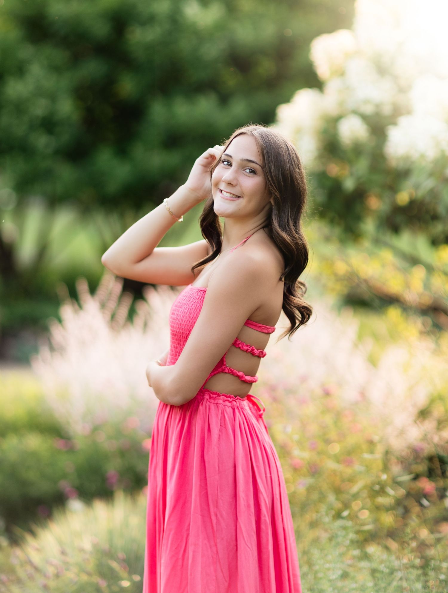 Young woman in hot pink maxi dress posing in garden with lush greenery and flowers.