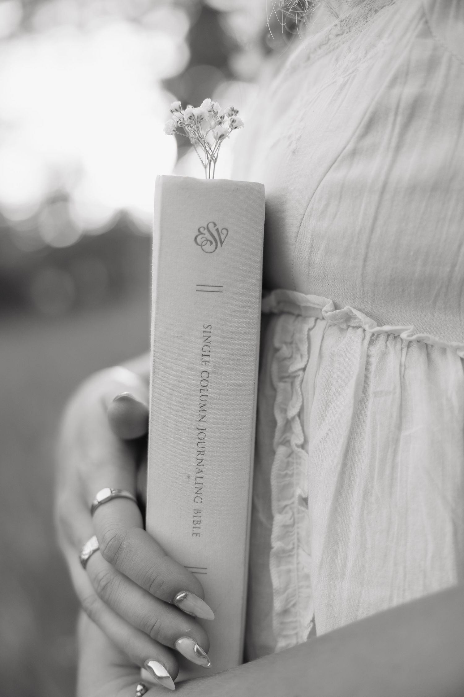 Black and white photo of woman holding ESV Single Column Journaling Bible with flowers.