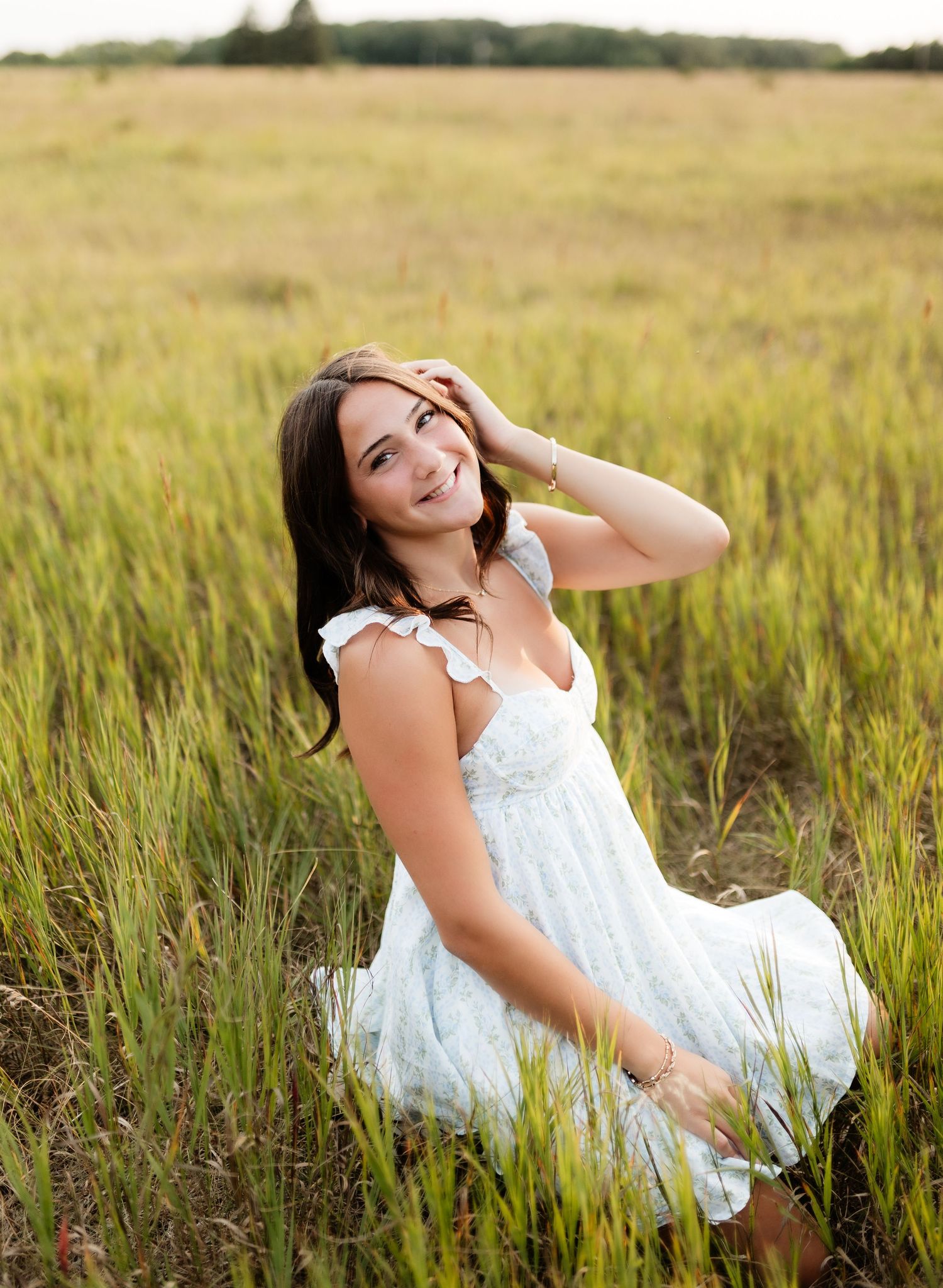 Smiling woman in white dress sitting in golden tall grass field.