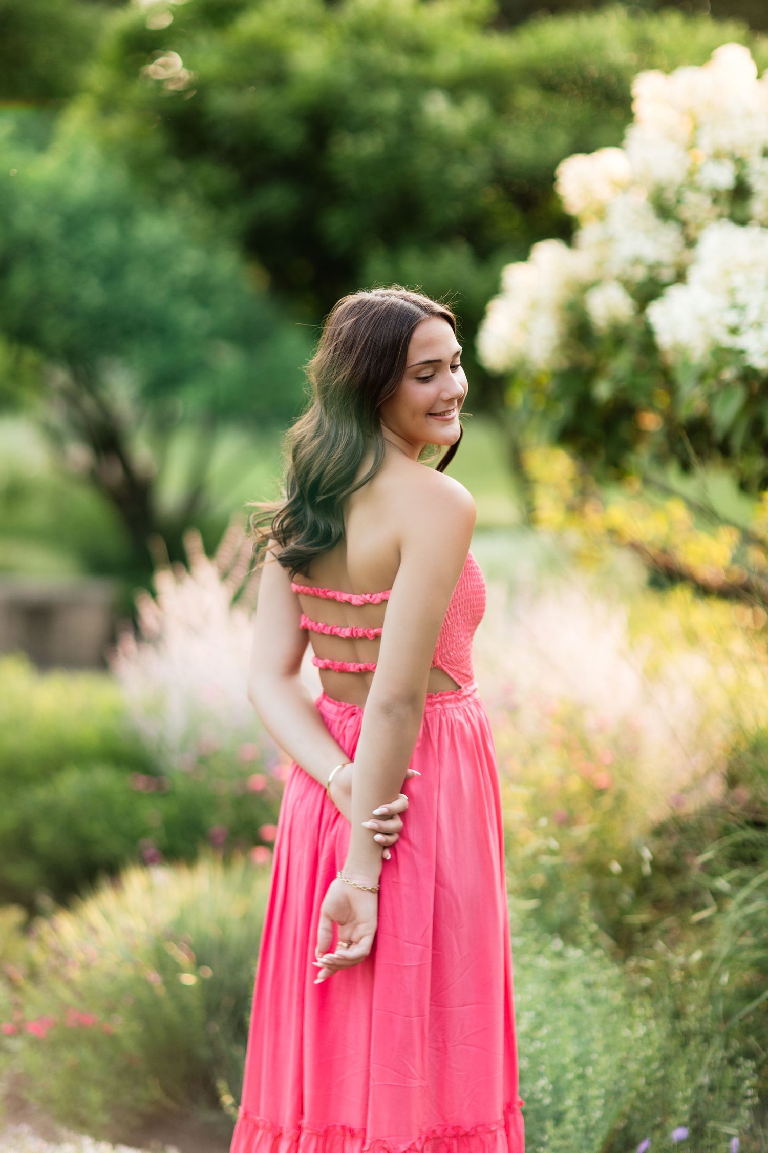 Young woman in a pink strapless dress with cutout back smiling over her shoulder in a garden.