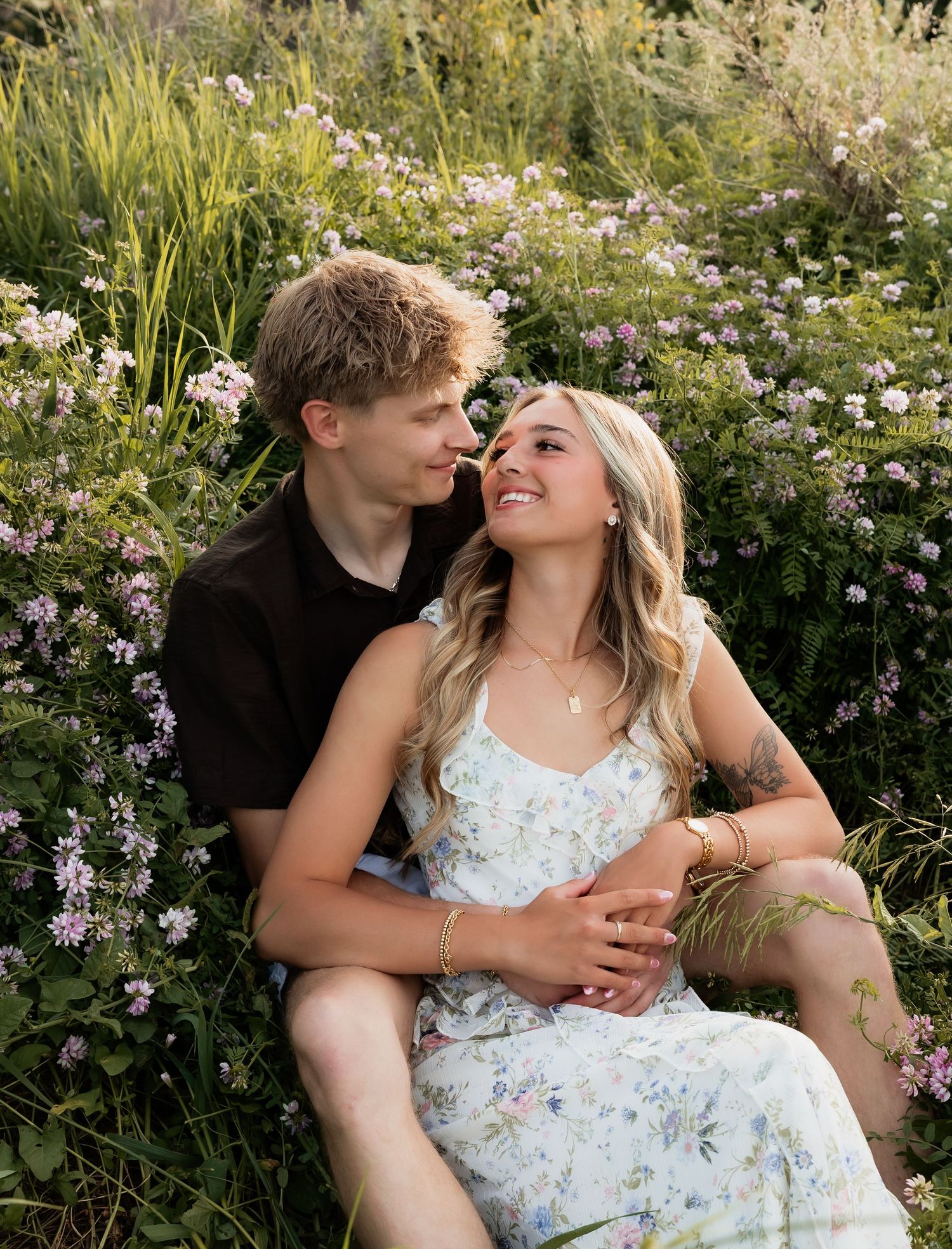 Romantic couple gazing at each other while sitting among blooming pink wildflowers outdoors.