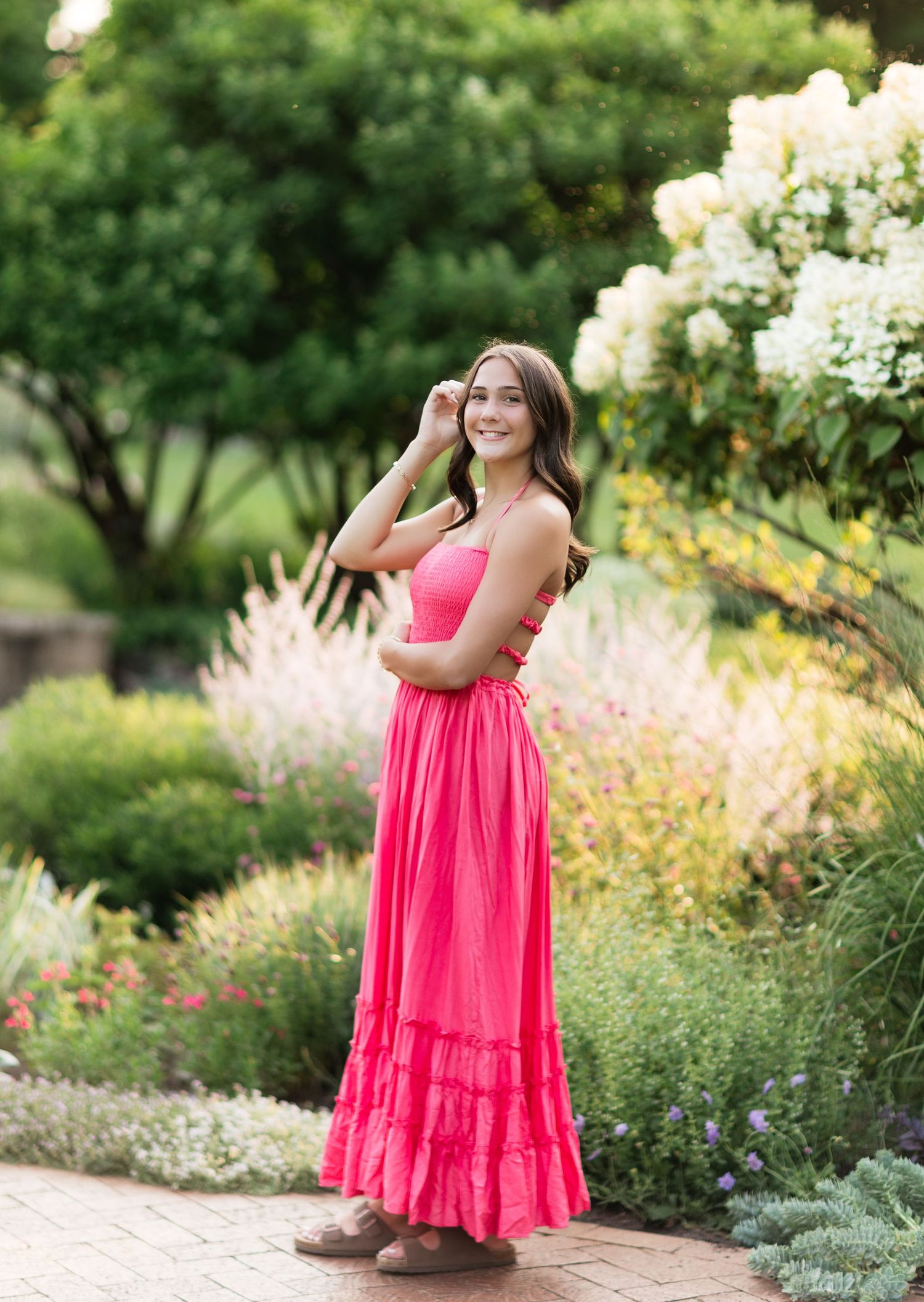 Brunette in vibrant pink strapless maxi dress with ruffle hem posing in blooming garden setting.