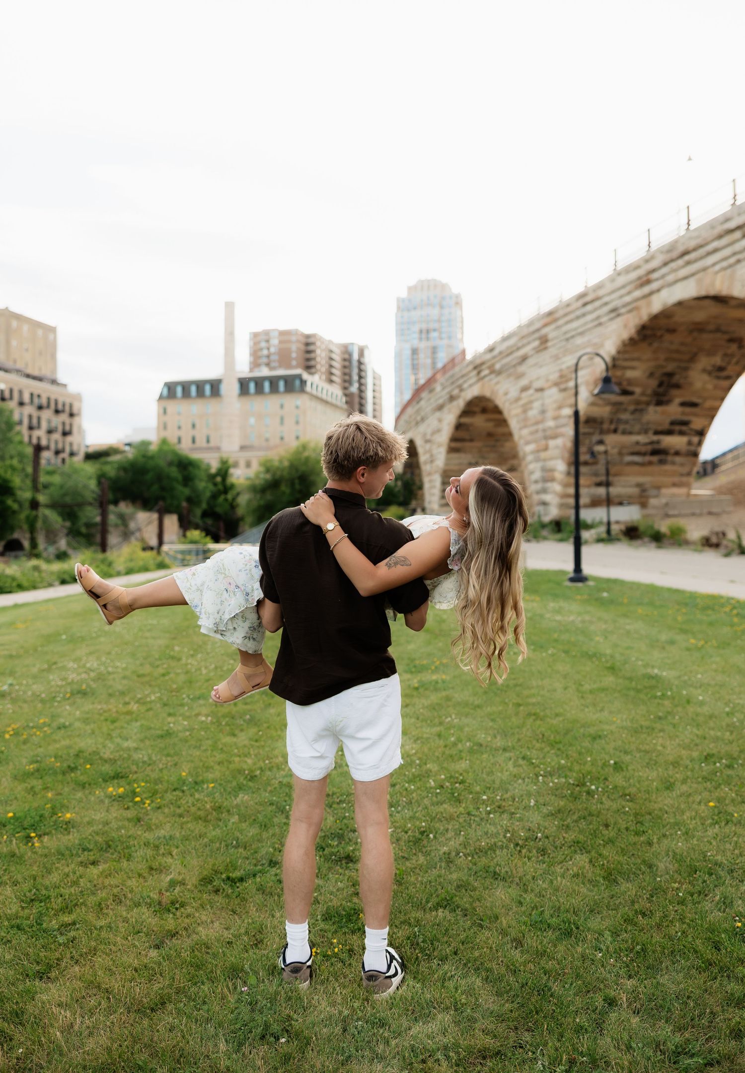 Romantic couple embrace as man lifts woman near historic Stone Arch Bridge in Minneapolis.