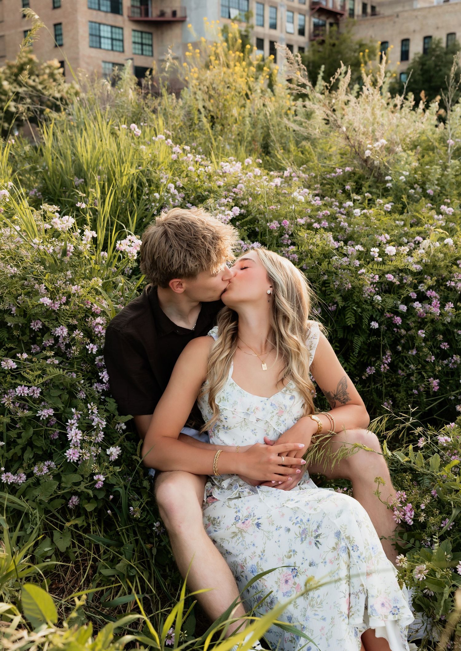 Romantic couple kissing while sitting among wildflowers and lush greenery in an urban garden.