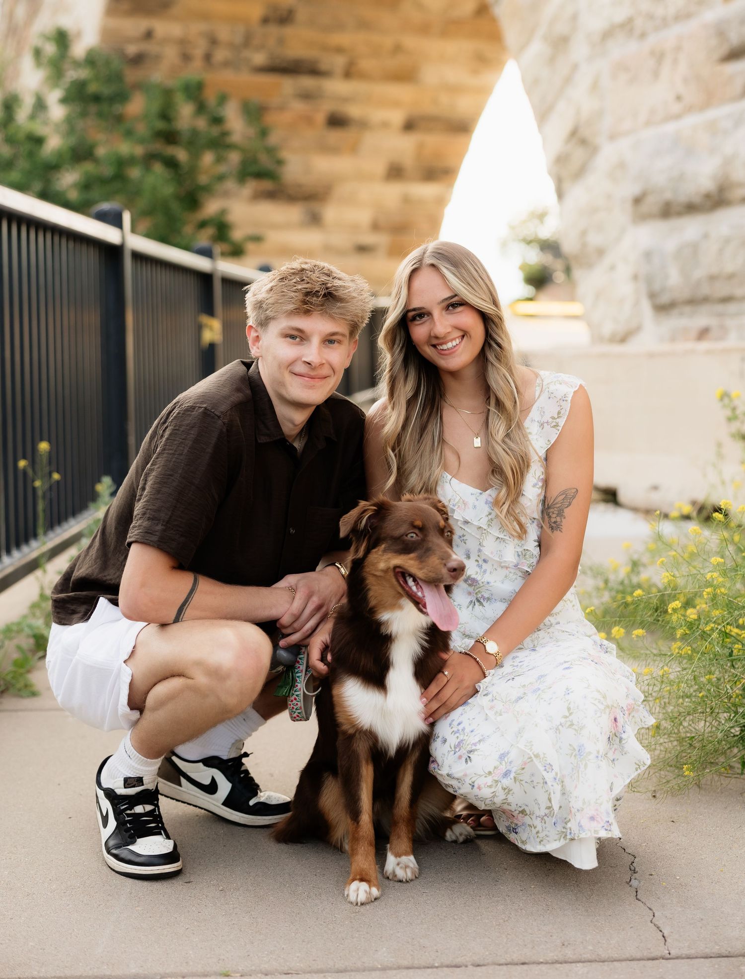 Young couple posing with their happy Australian Shepherd dog beneath a historic stone arch.