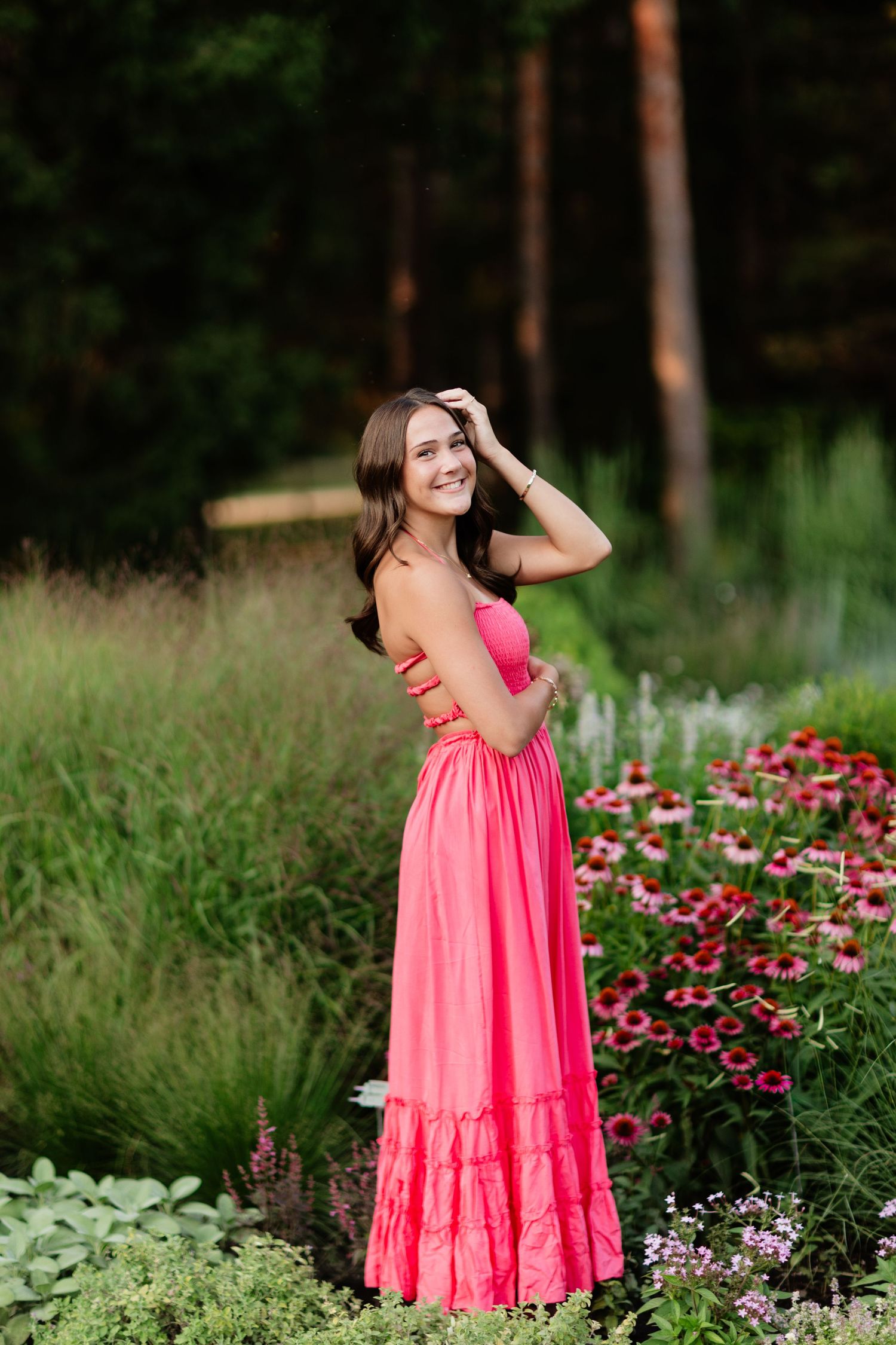 Young woman in coral pink maxi dress standing among vibrant red echinacea flowers in a garden.