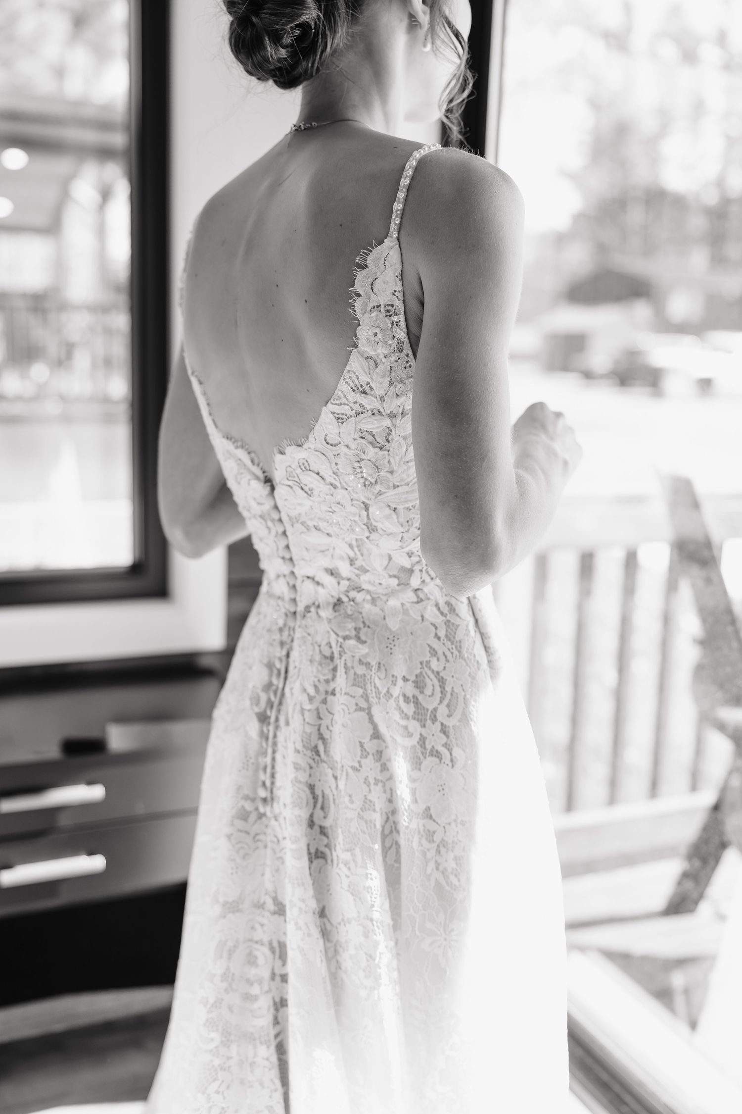 Black and white back view of bride in elegant lace wedding gown with low back and spaghetti straps.