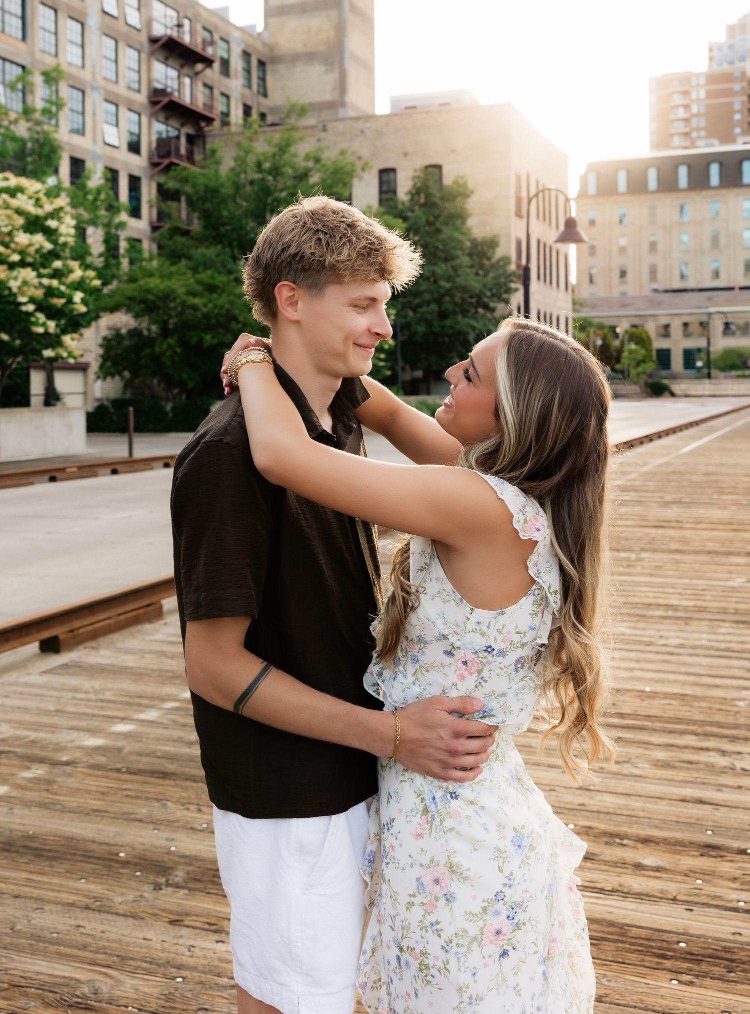 Young couple embracing and smiling at each other on a sunny wooden boardwalk in the city.