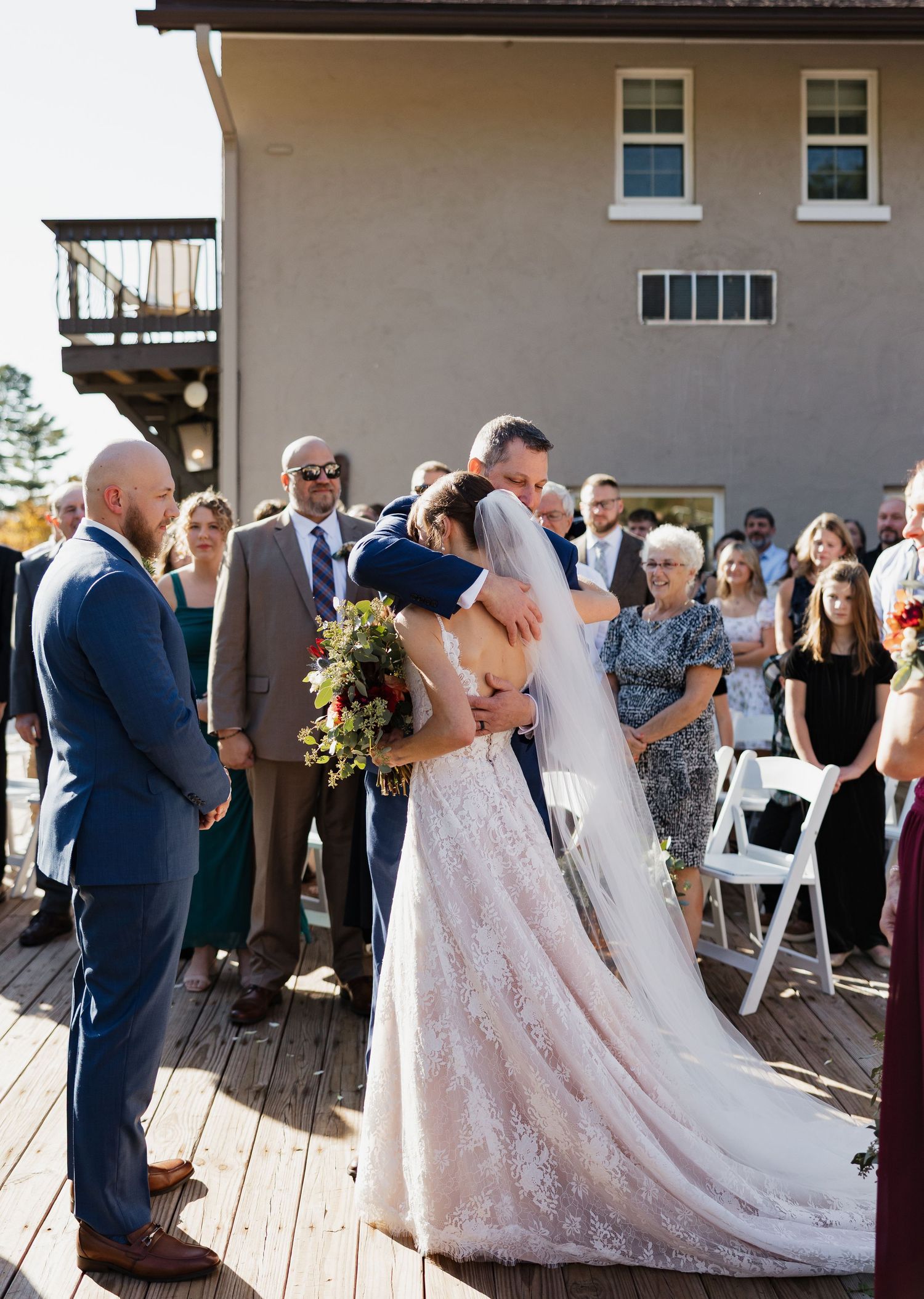 Bride and groom share emotional hug at outdoor wedding ceremony with guests watching.