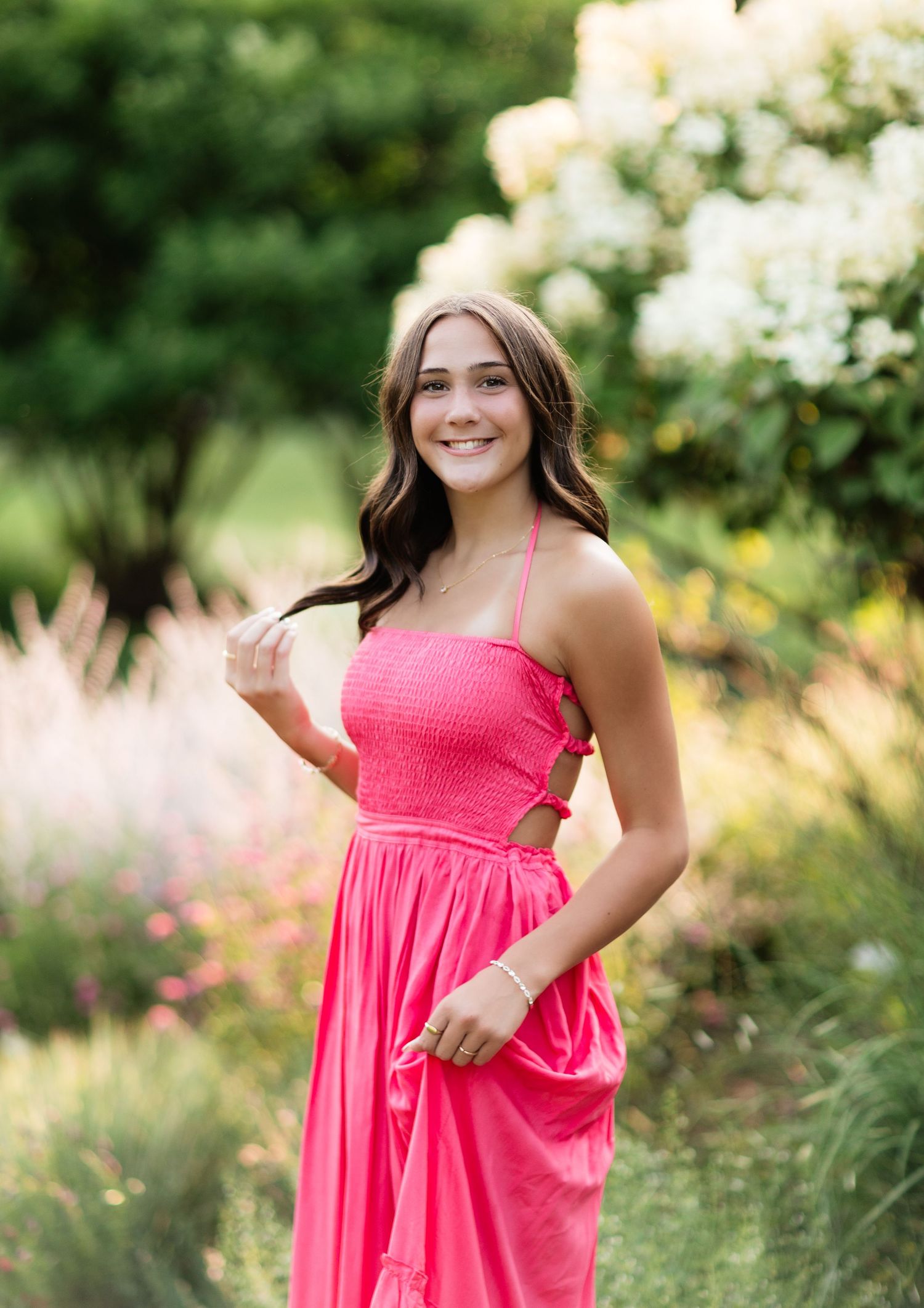 Smiling young woman in a bright pink halter dress posing in a lush summer garden.