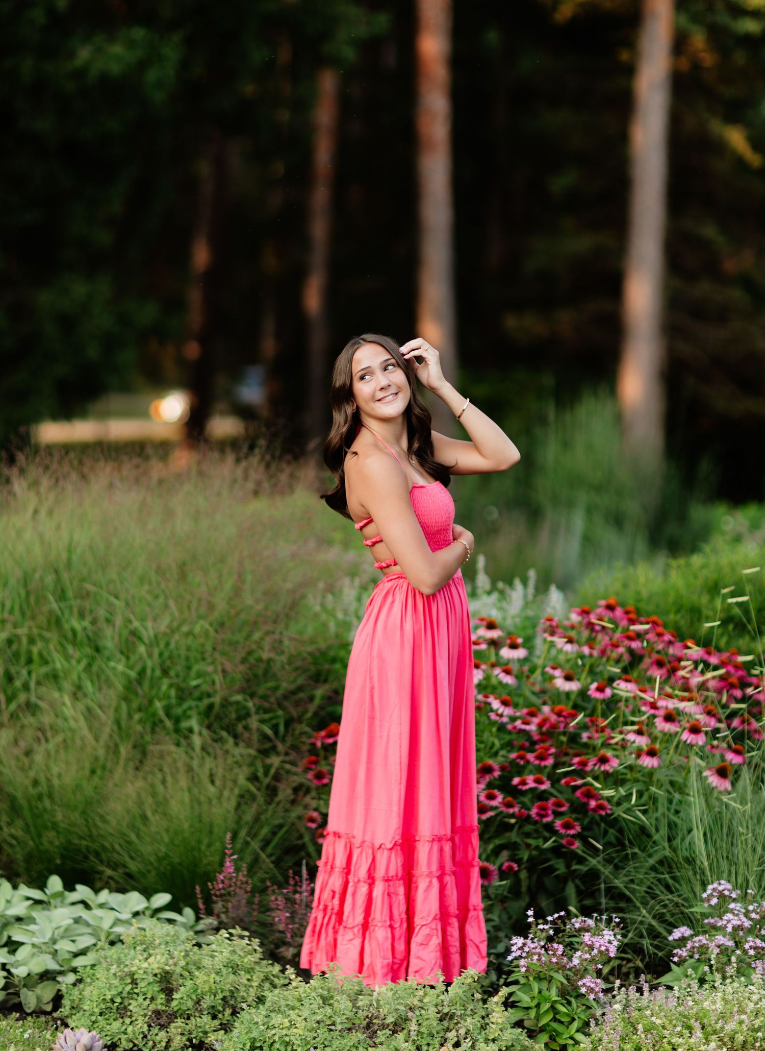 Woman in coral maxi dress standing among wildflowers in a garden.