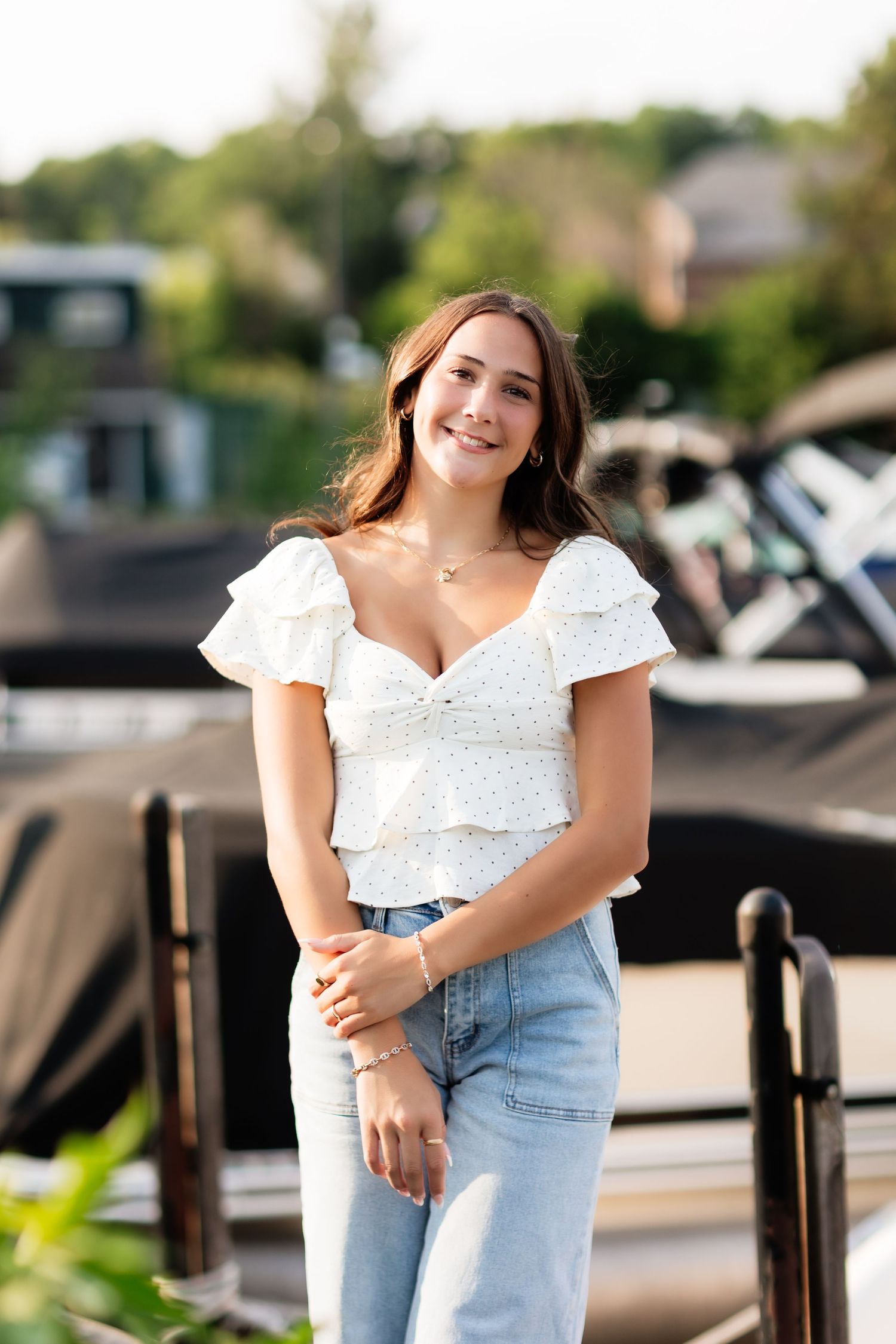 Smiling young woman in white ruffled crop top and jeans posing near marina on sunny day.