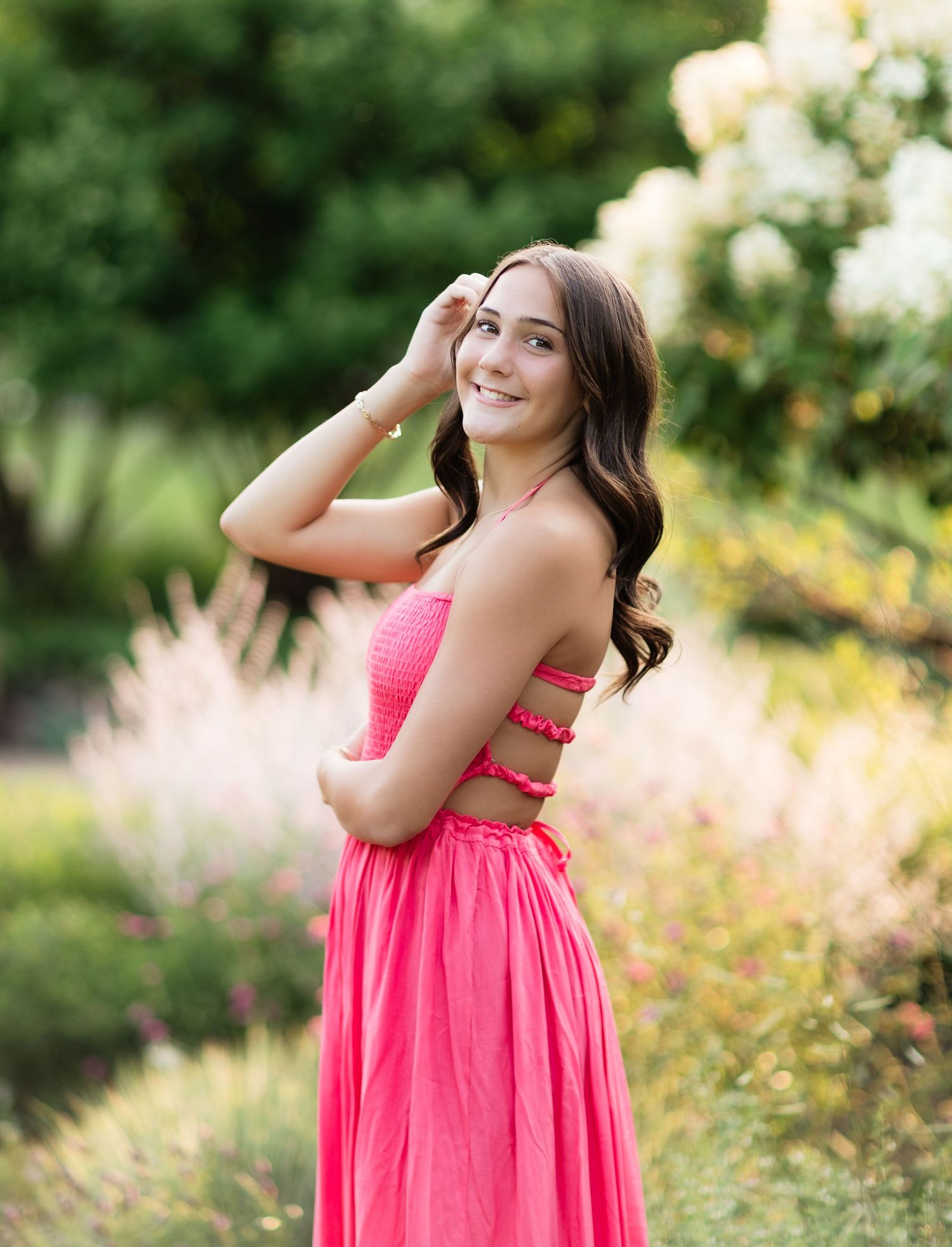 Smiling brunette in a pink halter maxi dress posing in a colorful garden setting.