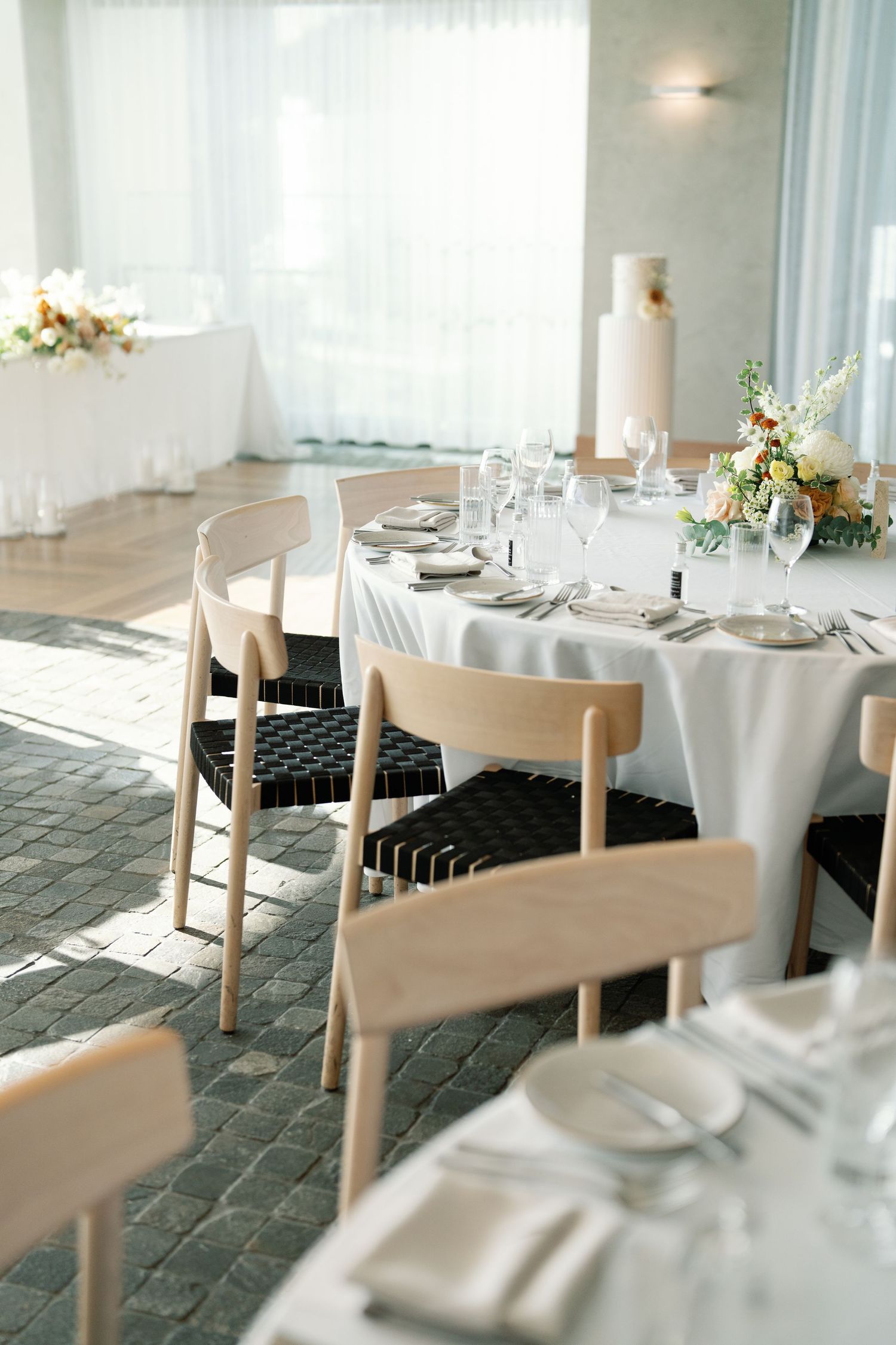 Modern restaurant interior with white tablecloths and wooden chairs in natural lighting.