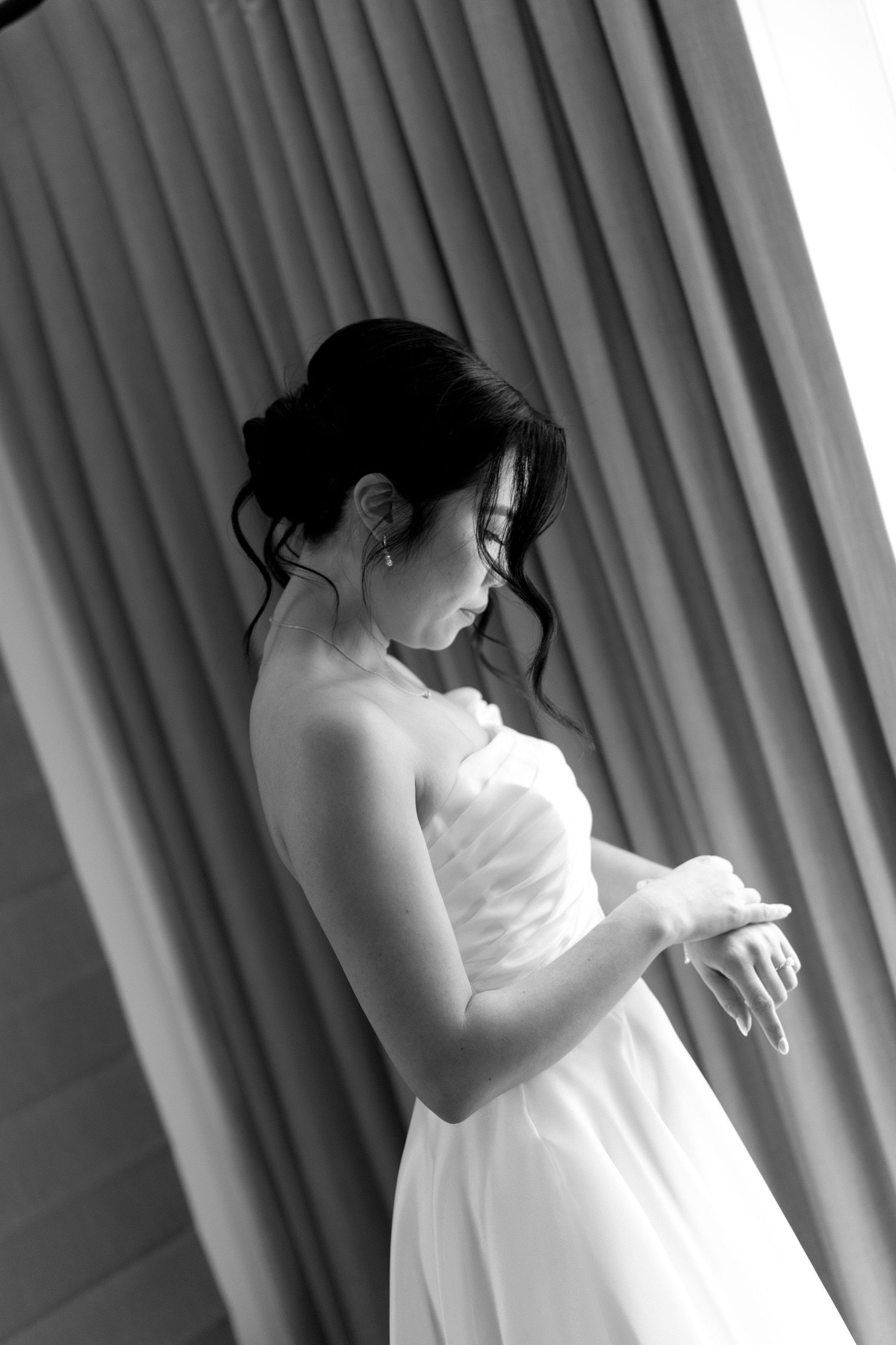 Bride getting ready in a white dress with dramatic lighting and curtains in the background.