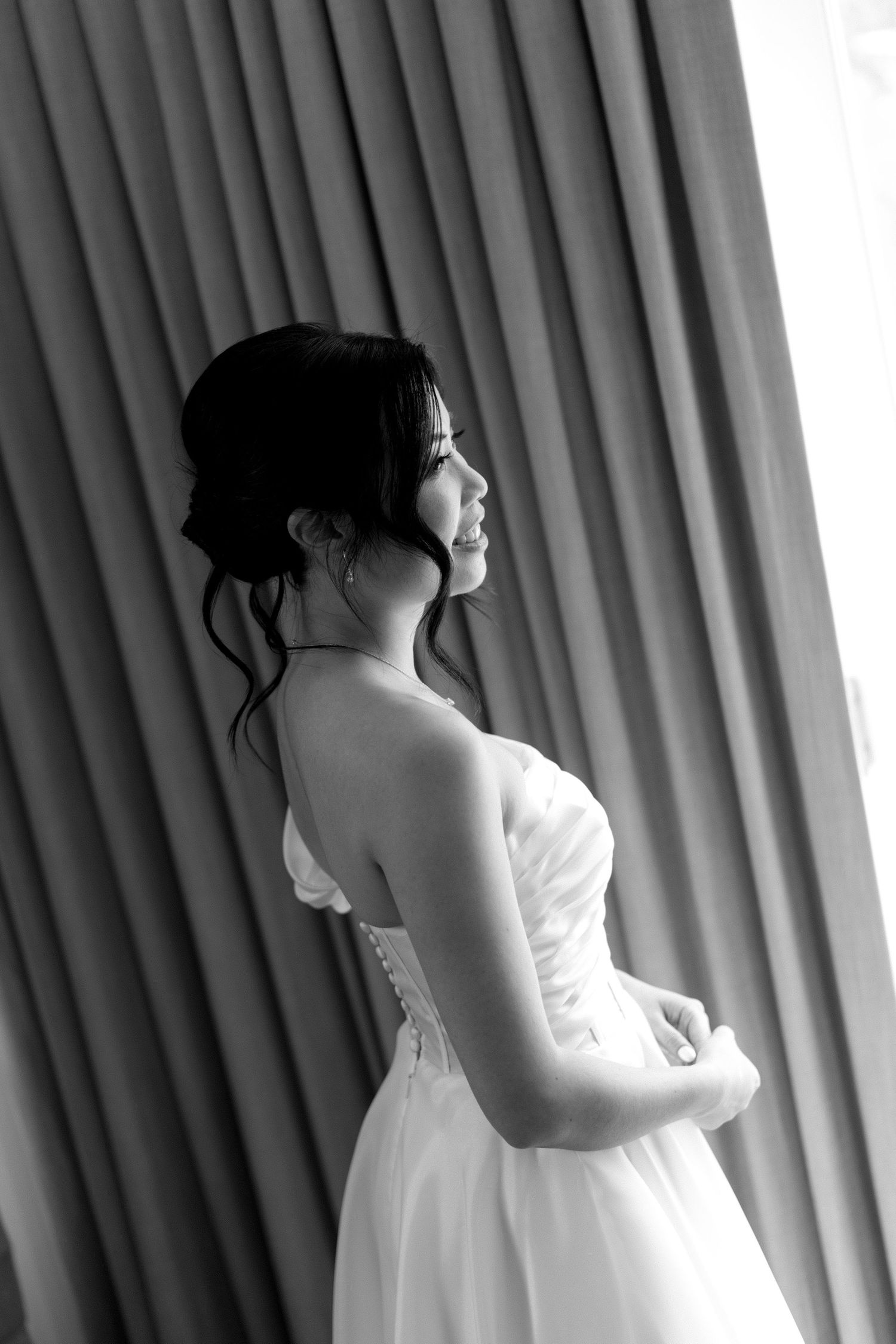 Black and white portrait of a bride in a strapless wedding gown looking to the side against a curtained background.