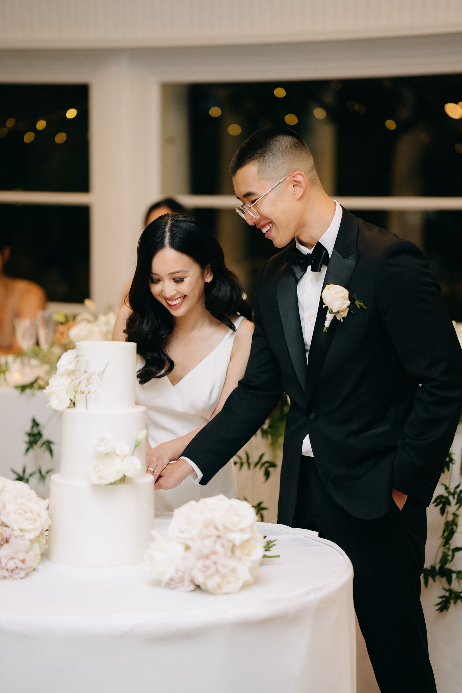 Couple cutting their elegant white wedding cake adorned with flowers.