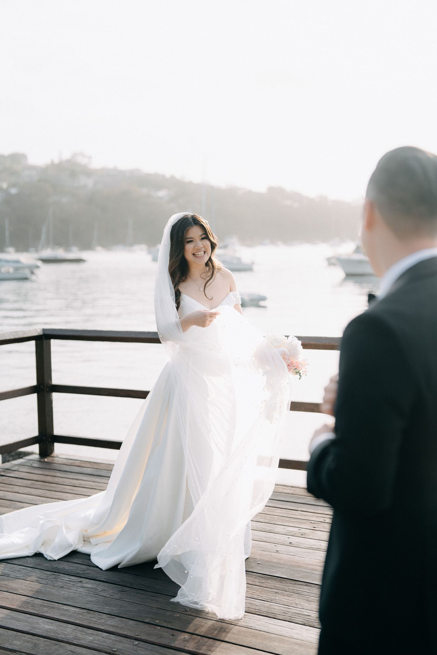 Newlywed couple sharing intimate moments on wooden dock by the water.