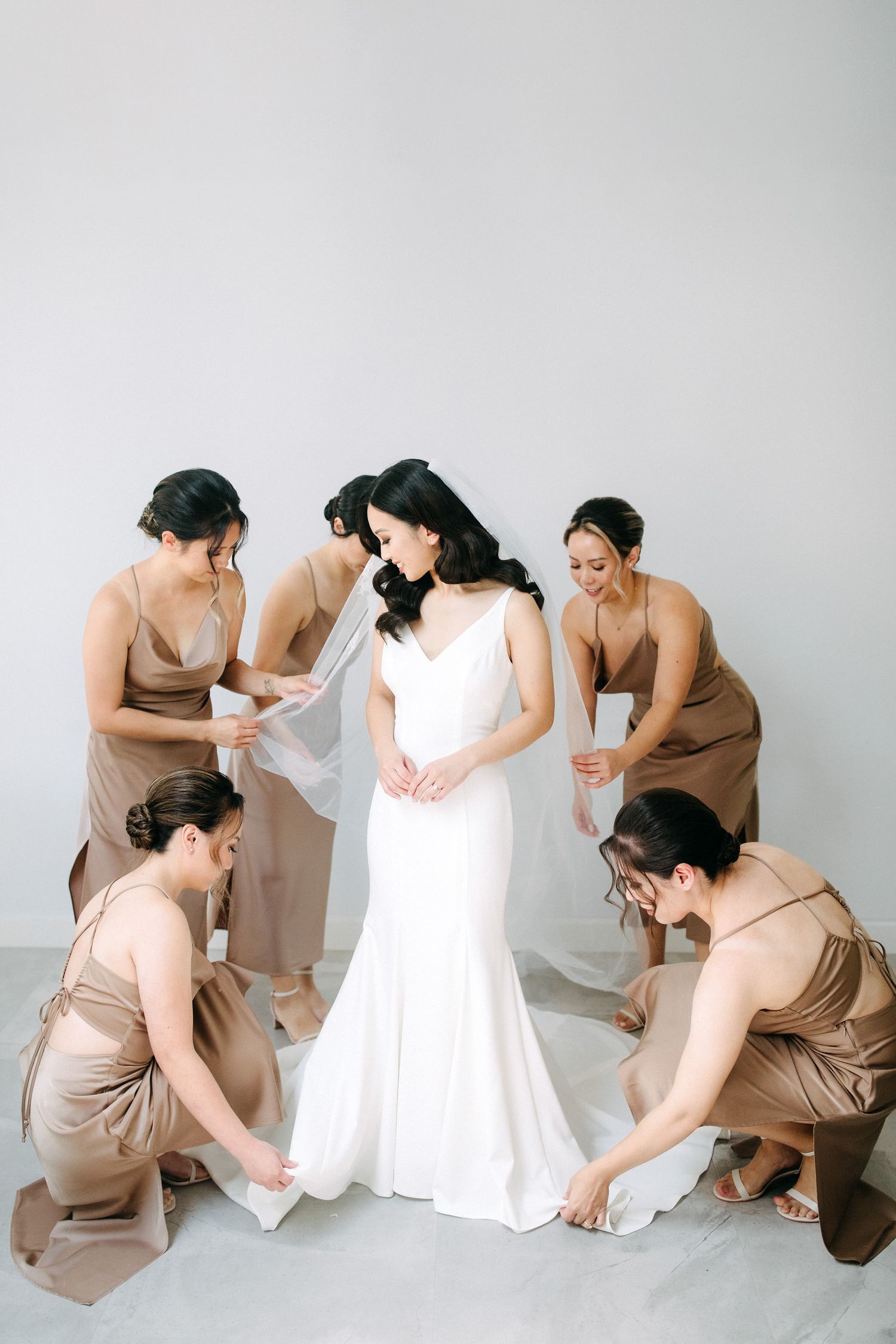 Bridesmaids in beige dresses helping adjust the bride's white gown.
