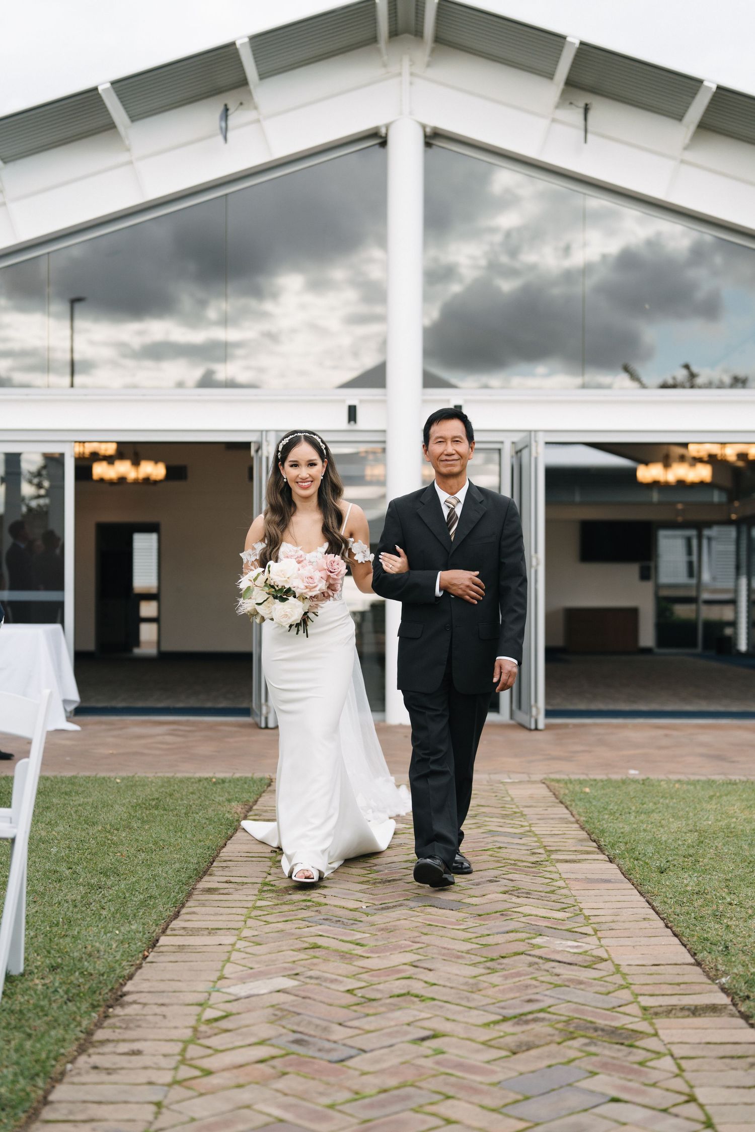 A wedding ceremony procession walking down a stone path outside a white tent structure.