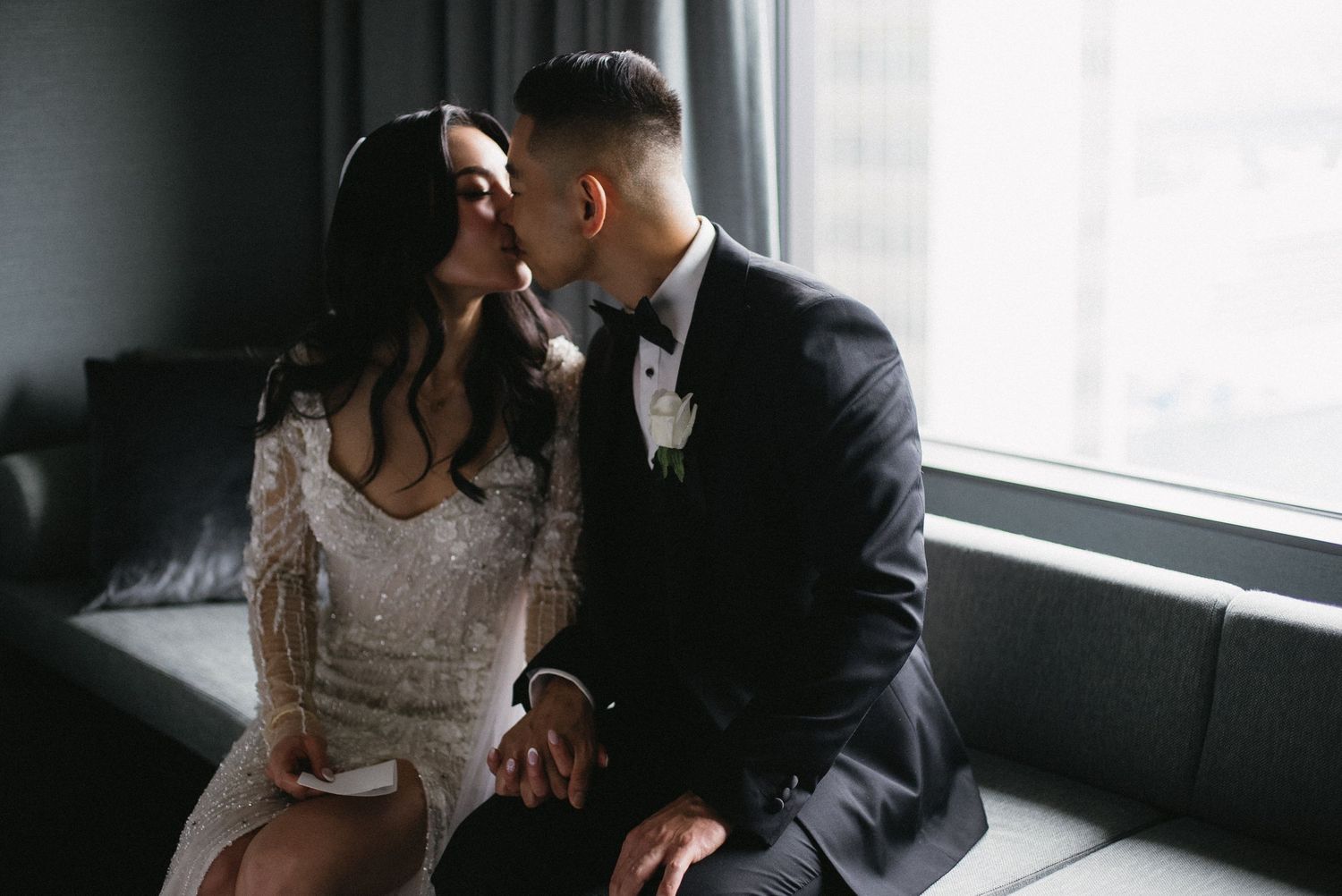 A romantic couple shares an intimate moment while sitting together by a window in elegant wedding attire.