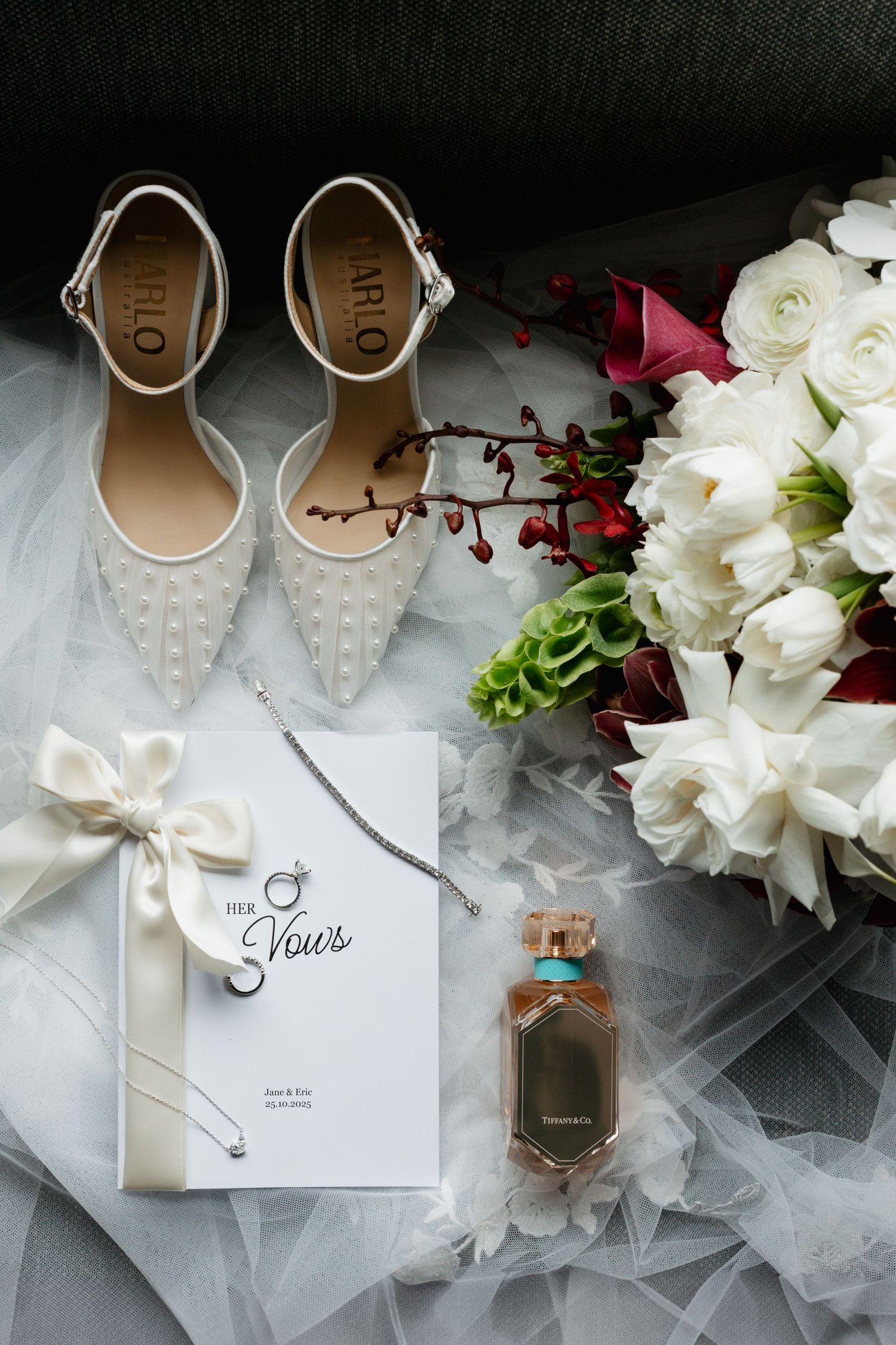 Wedding details flatlay with white shoes, invitation, flowers and perfume.