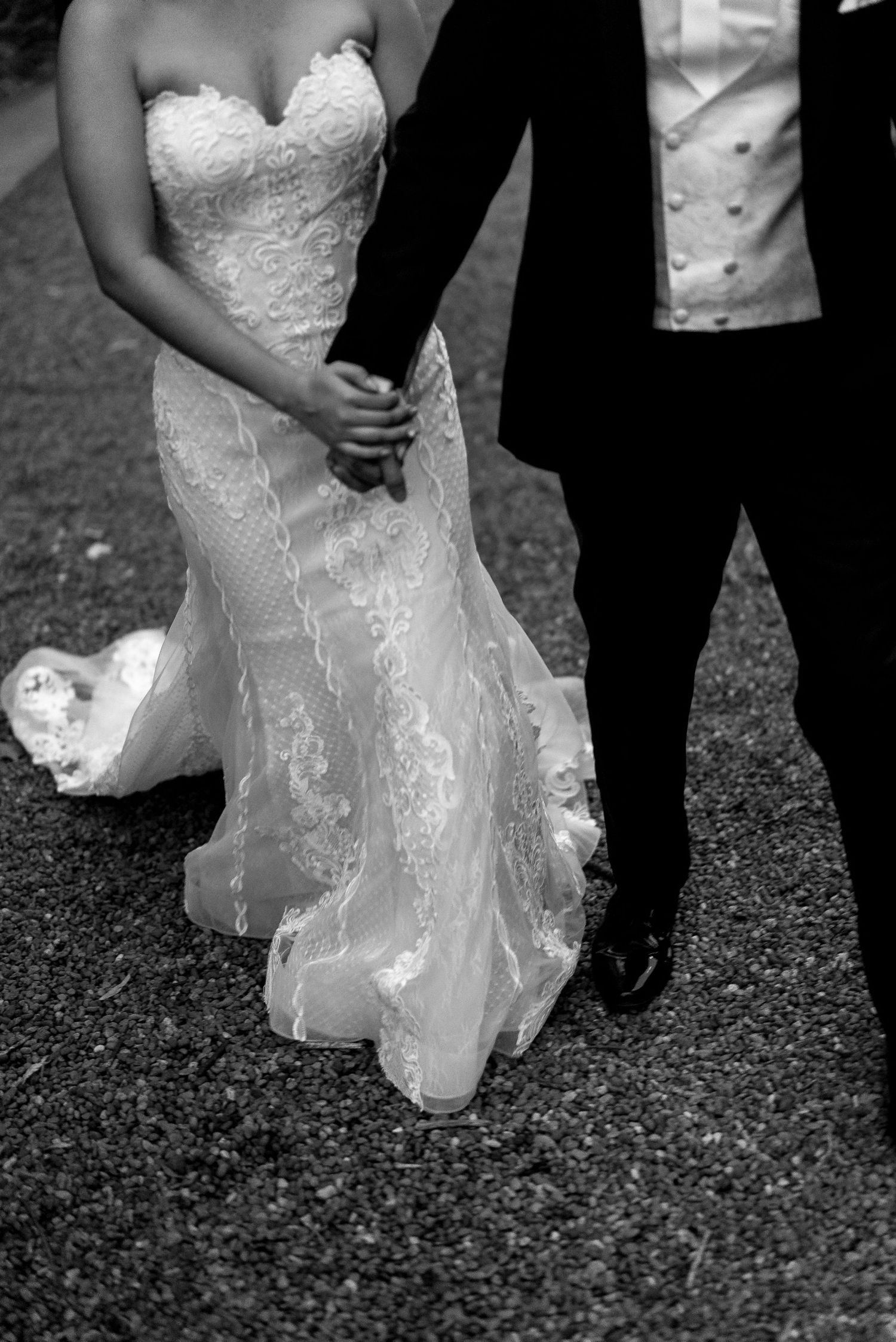 Black and white wedding photo showing the hem of a lace bridal gown against dark ground.
