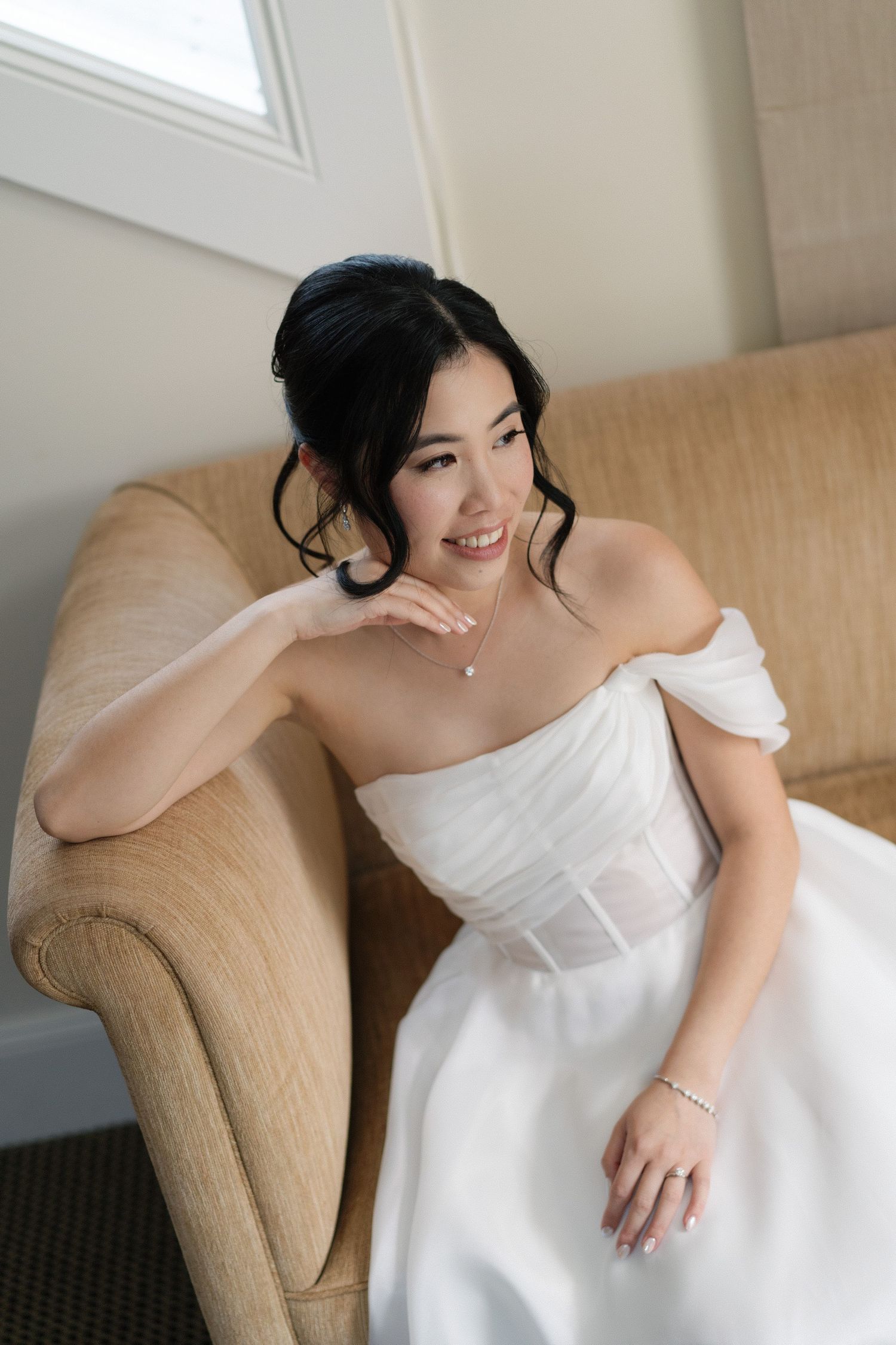 A bride in a white strapless wedding dress reclines gracefully on a beige armchair in a series of candid poses.