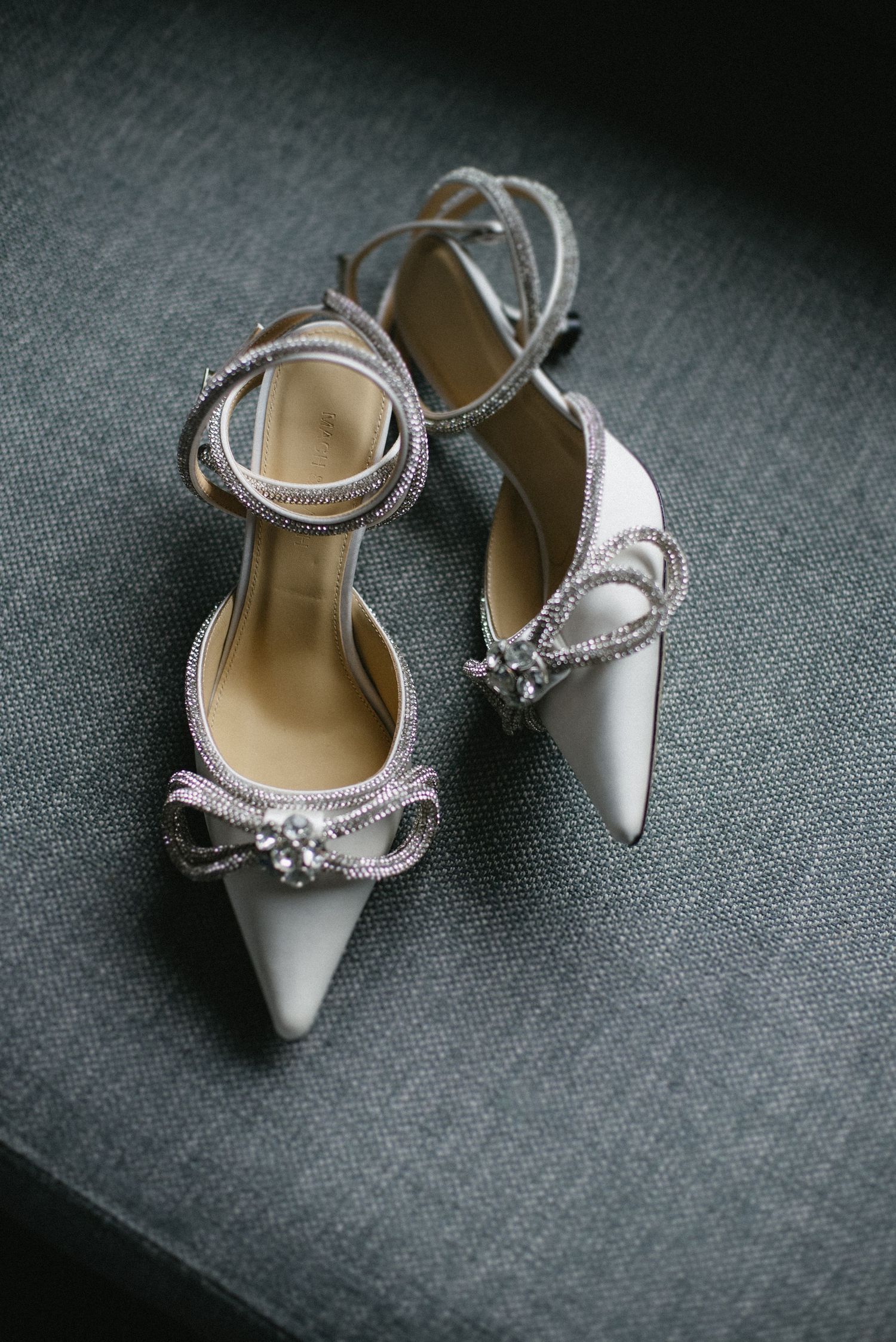 Elegant white bridal shoes with crystal embellishments displayed on a gray textured background in different angles.