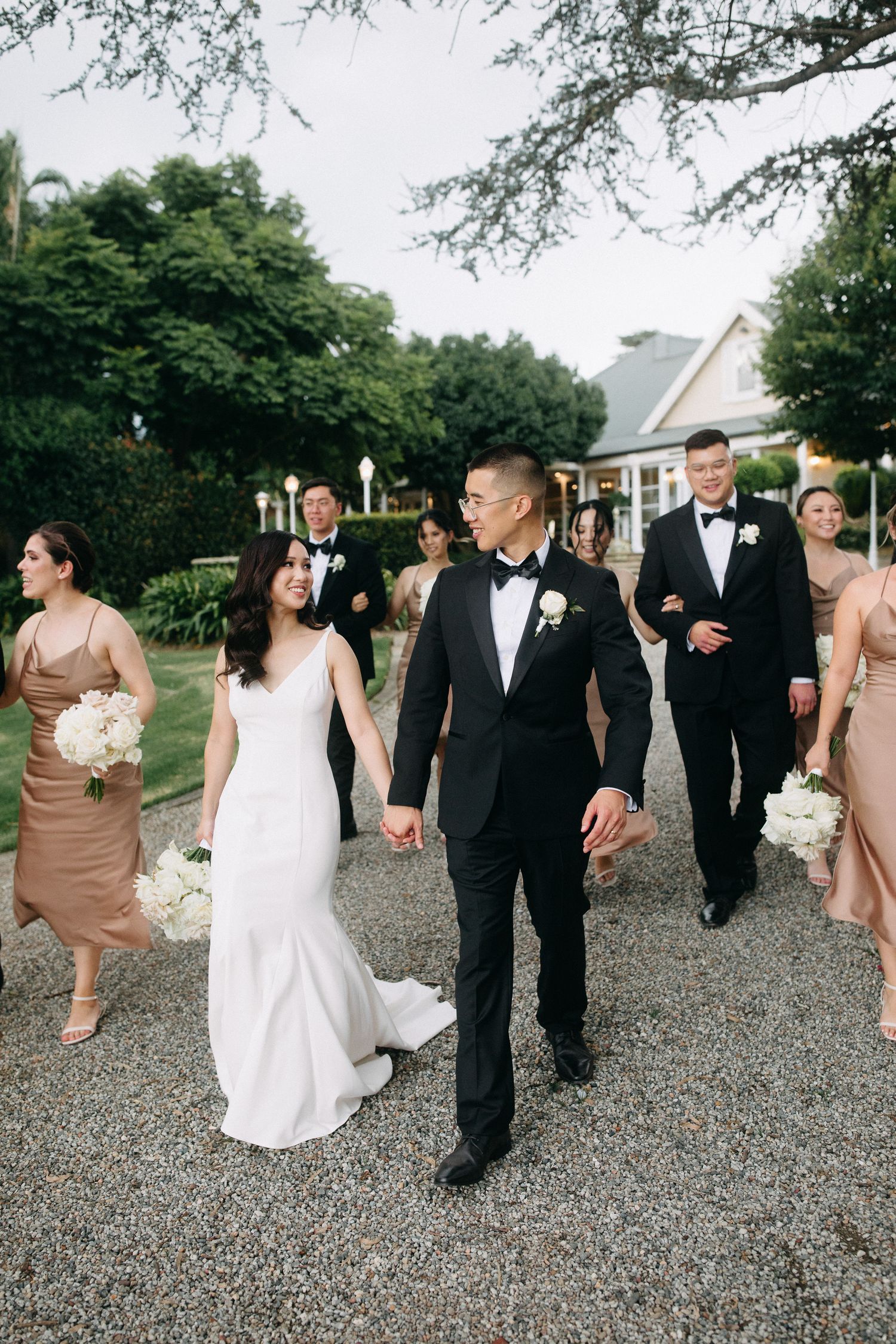 Wedding party walking together on a gravel path surrounded by greenery.