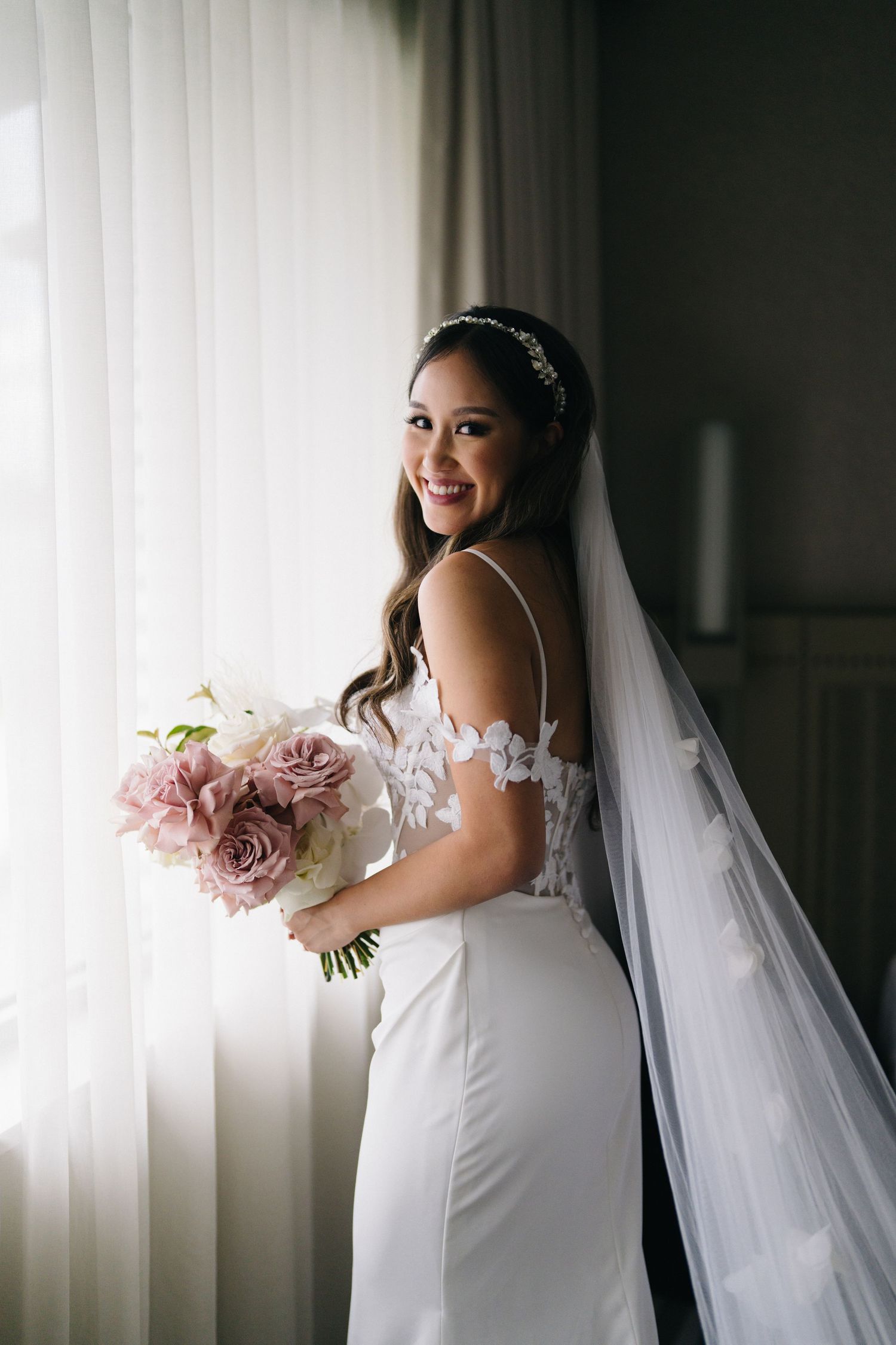 Elegant bridal portraits with flowing veil against white curtain backdrop.