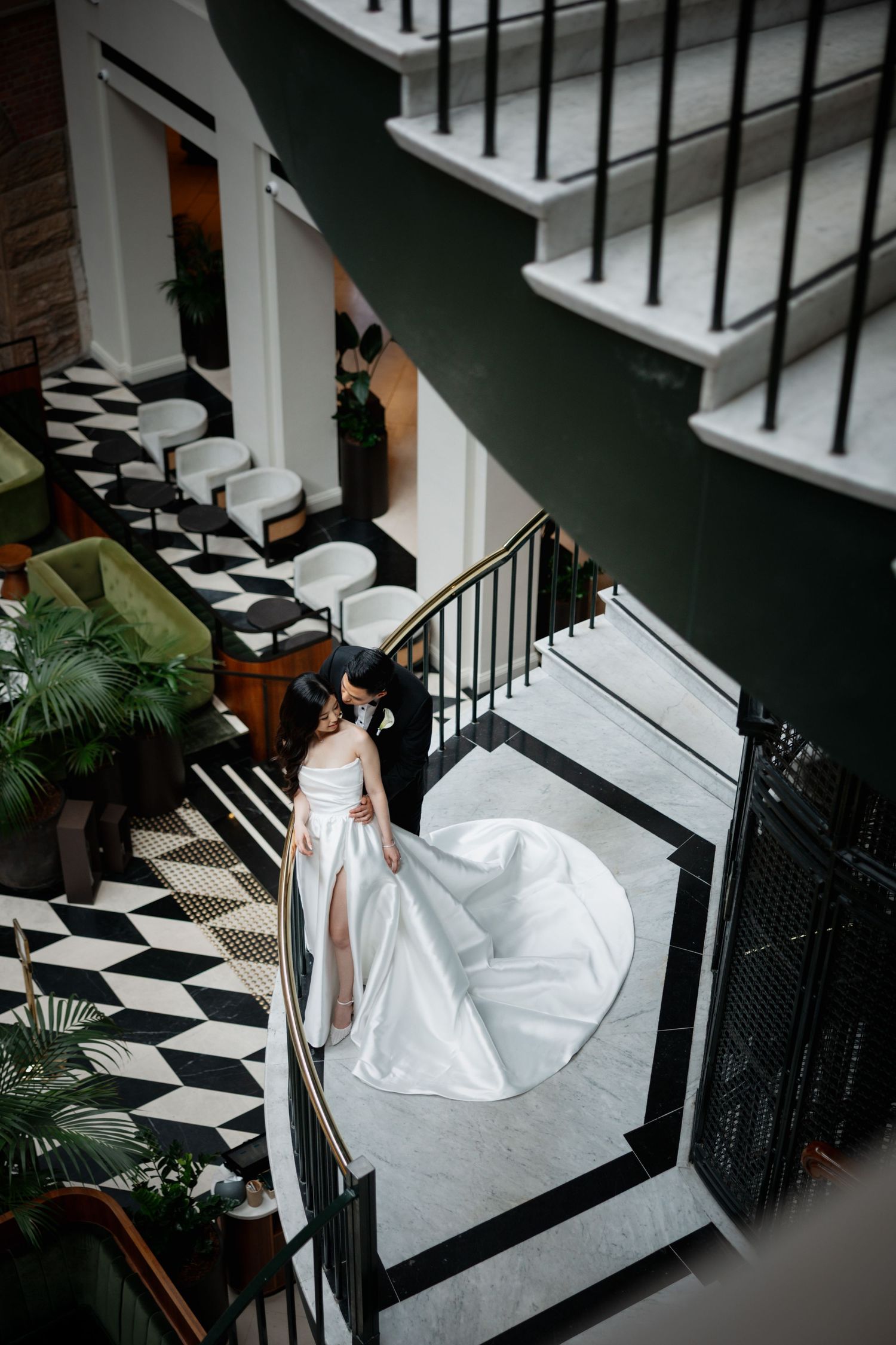 Elegant bride in flowing white gown descends a dramatic black and white staircase with iron railings.