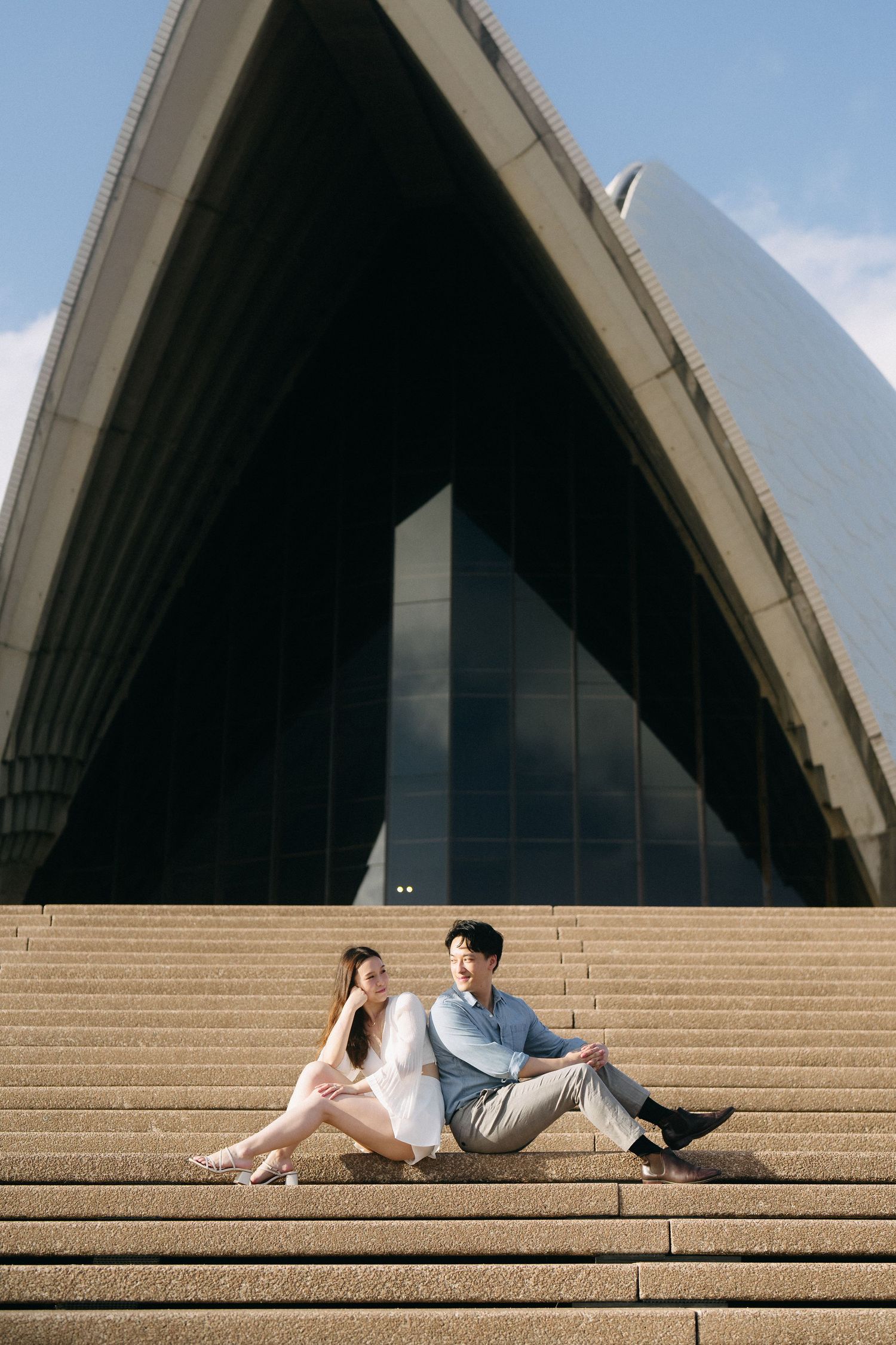 A couple relaxes on the iconic Sydney Opera House steps on a sunny day.