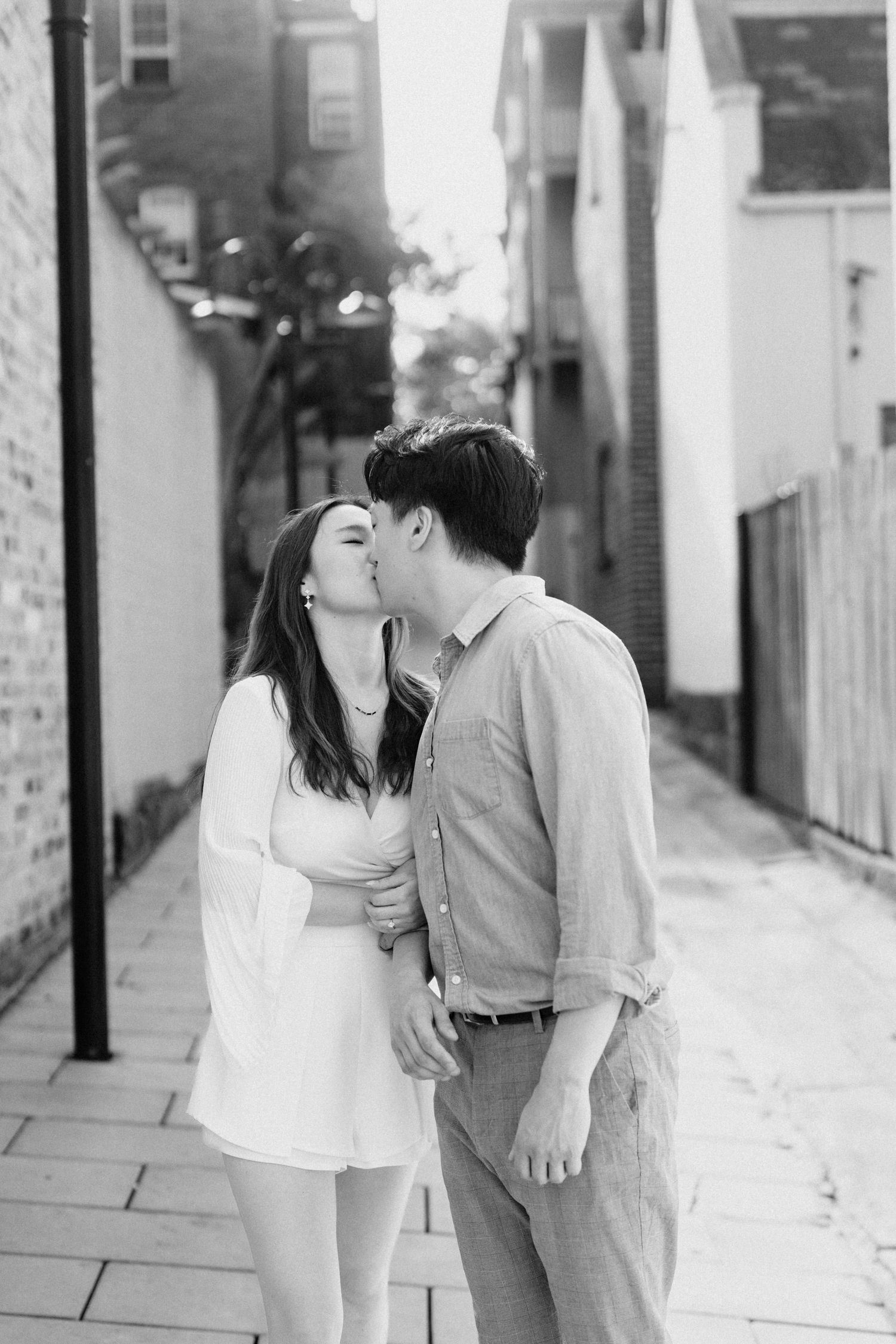 A couple shares intimate moments in a white alleyway setting.