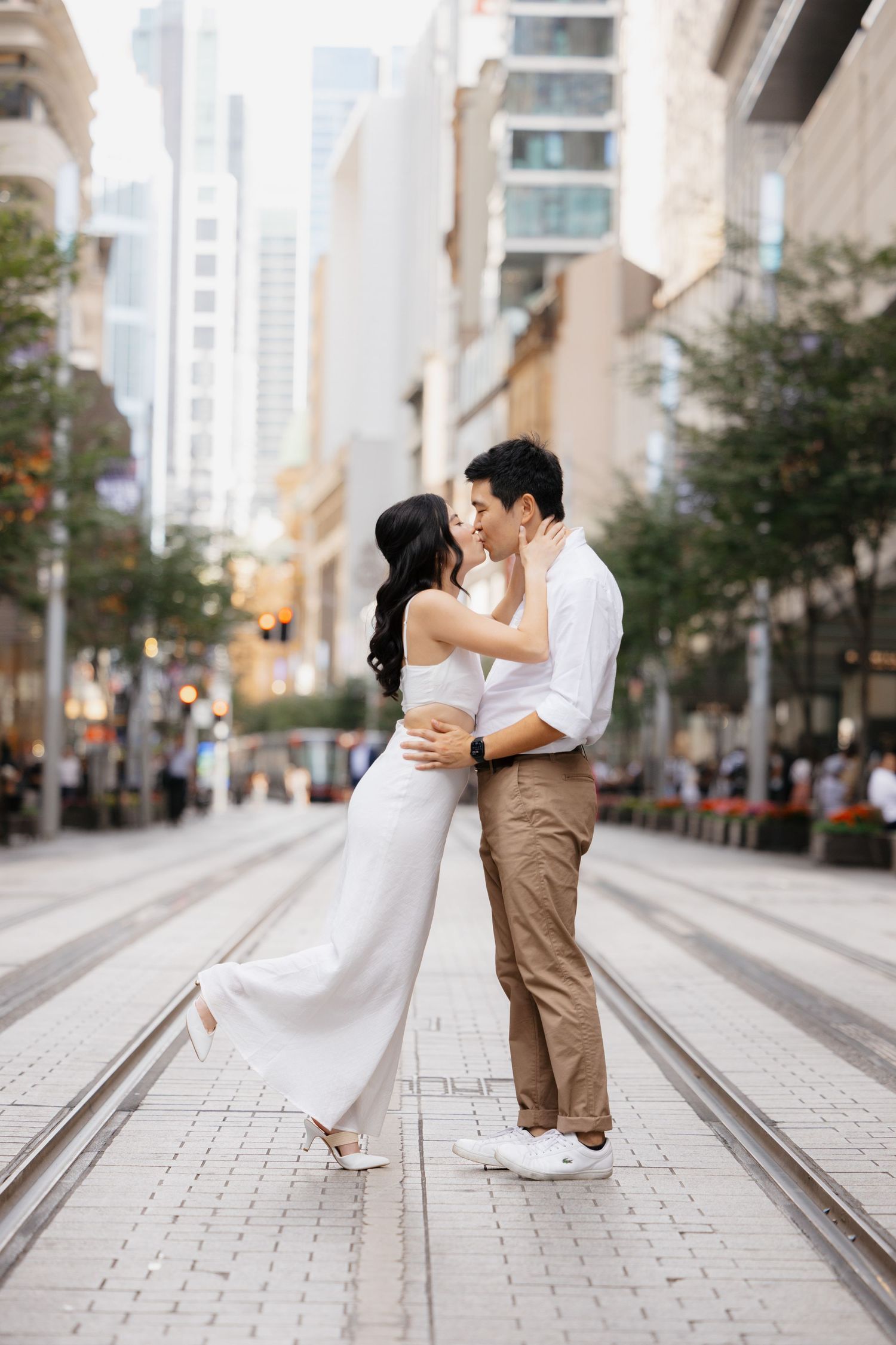 Romantic couple in wedding attire posing on urban street with tram tracks.