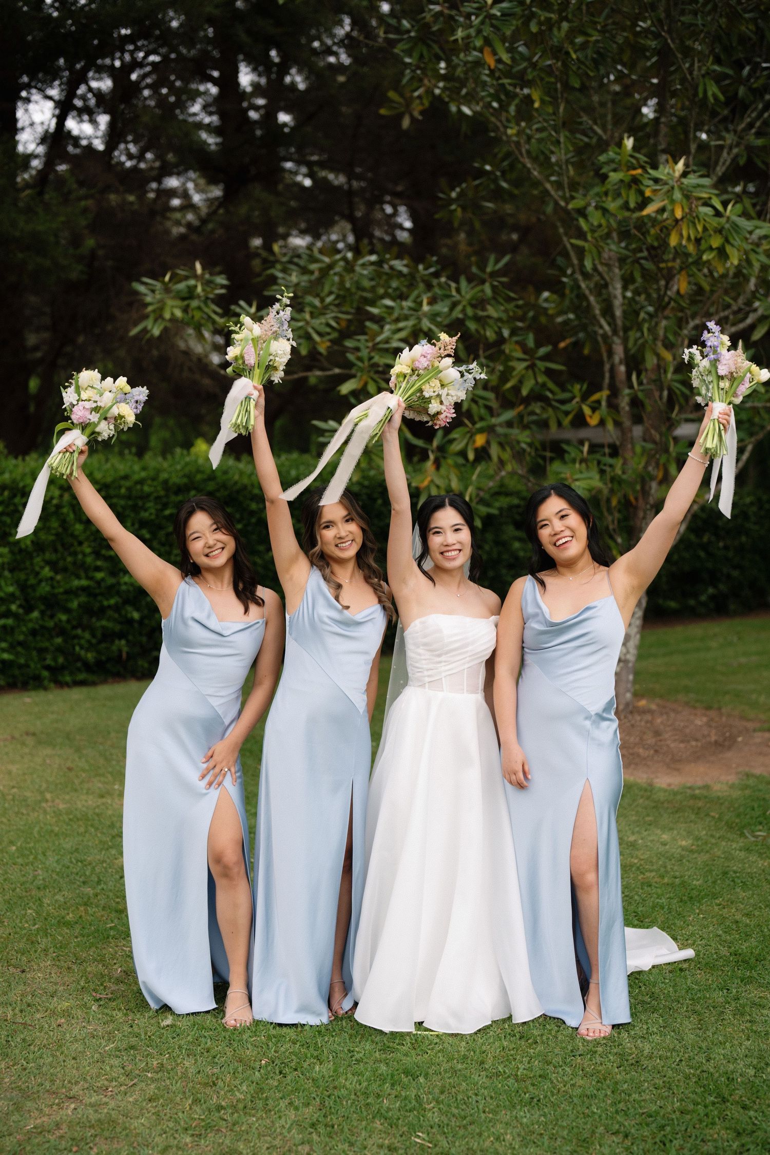A group in light blue bridesmaid dresses and a bride in white pose together on a grassy lawn during a wedding celebration.