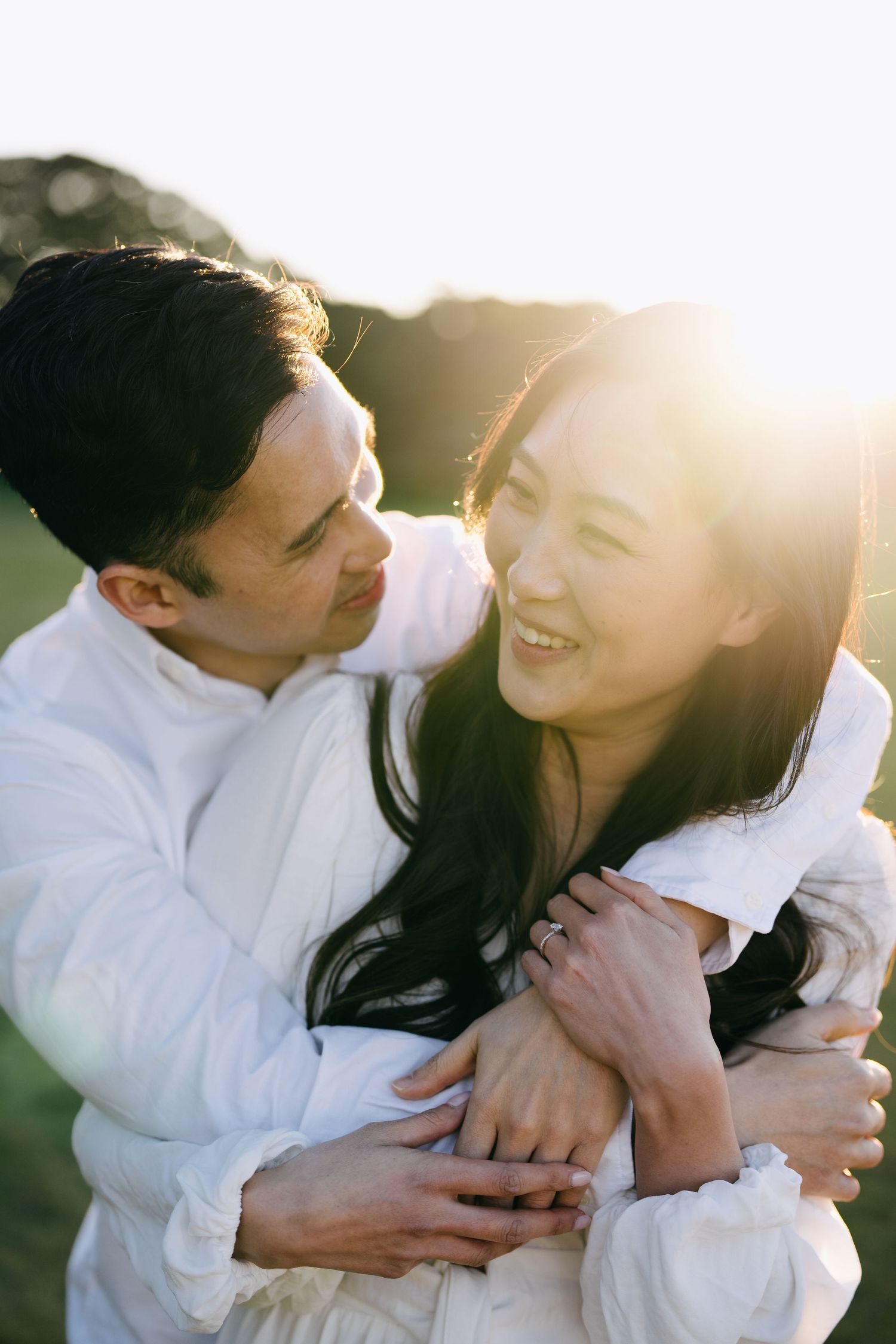 Intimate couple shares tender moments in white clothing against sunlit backdrop.