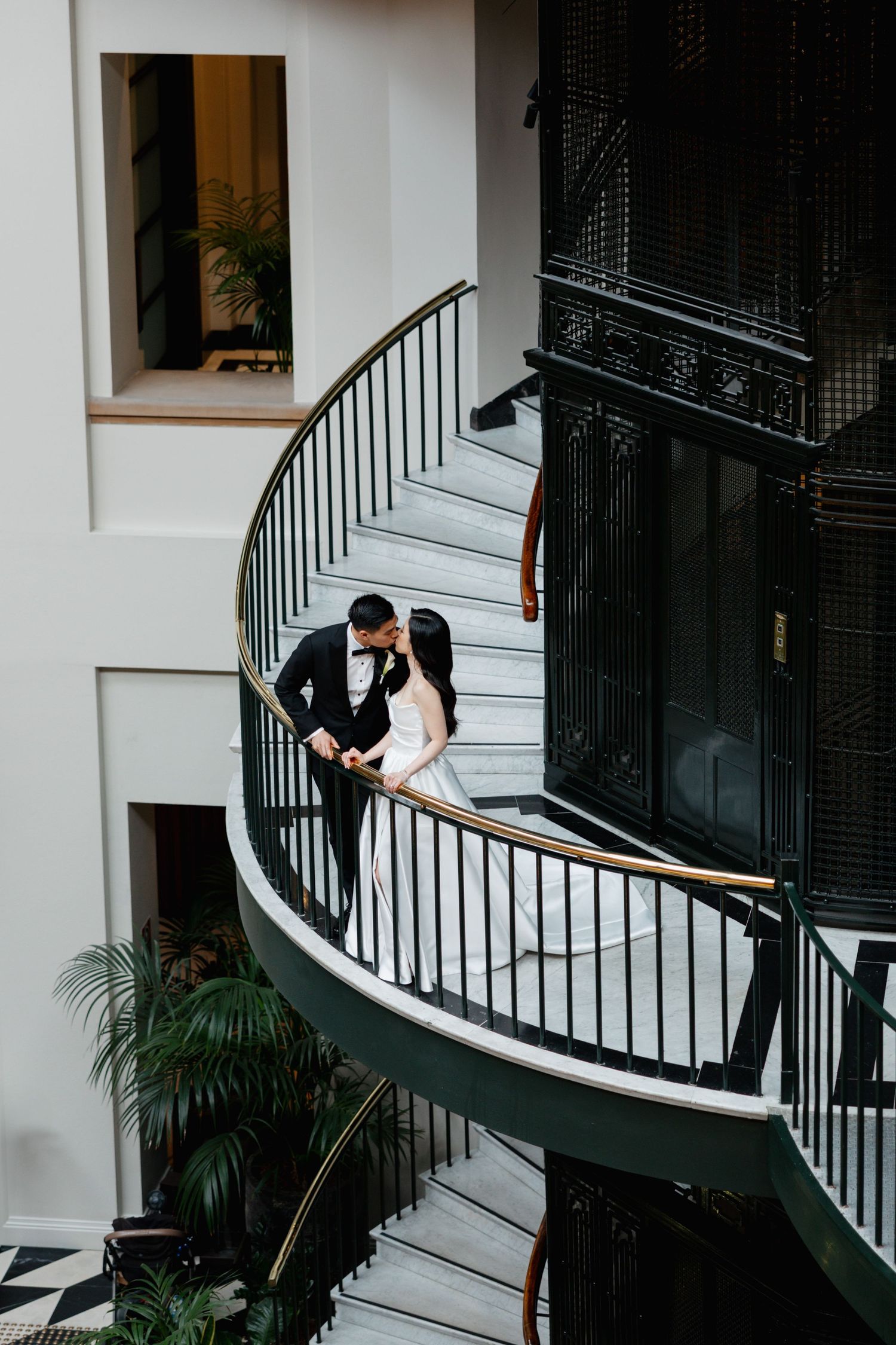 Wedding couple poses on elegant curved white staircase with black railings.