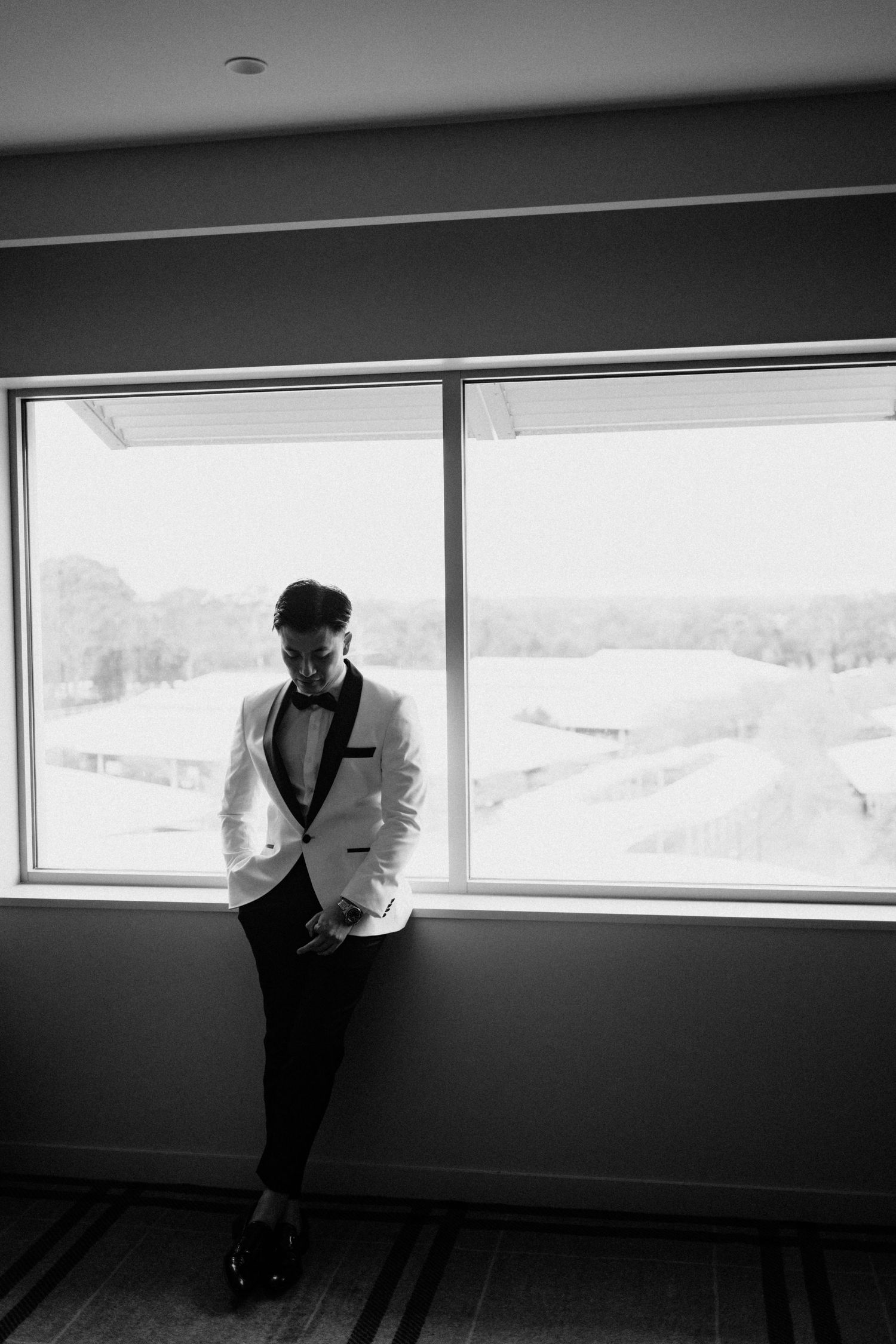 Artistic black and white photo of person in white suit jacket by window.