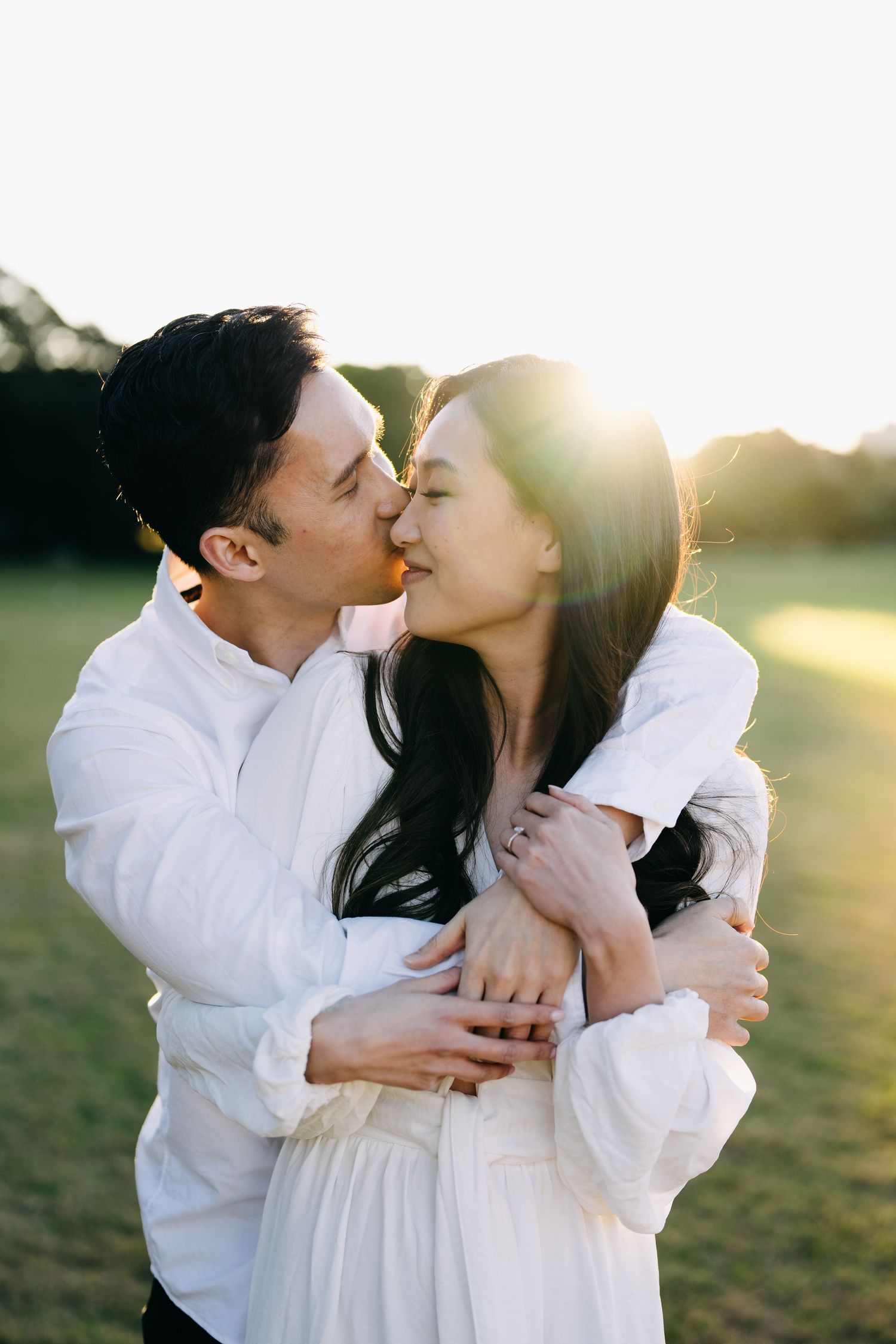A couple embraces in white outfits during a golden sunset photoshoot.