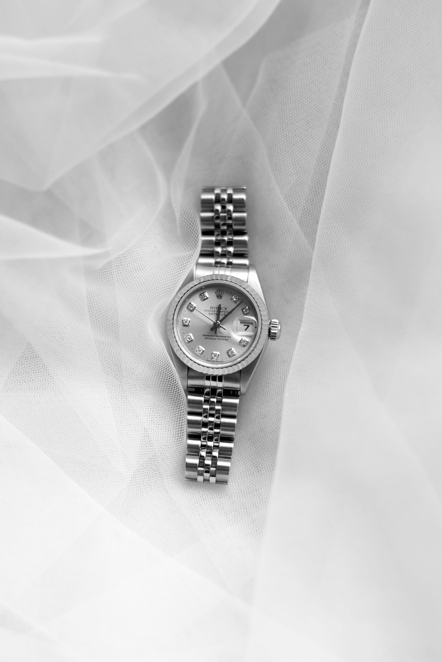 A silver stainless steel wristwatch with a classic Jubilee bracelet photographed on a soft white fabric background.