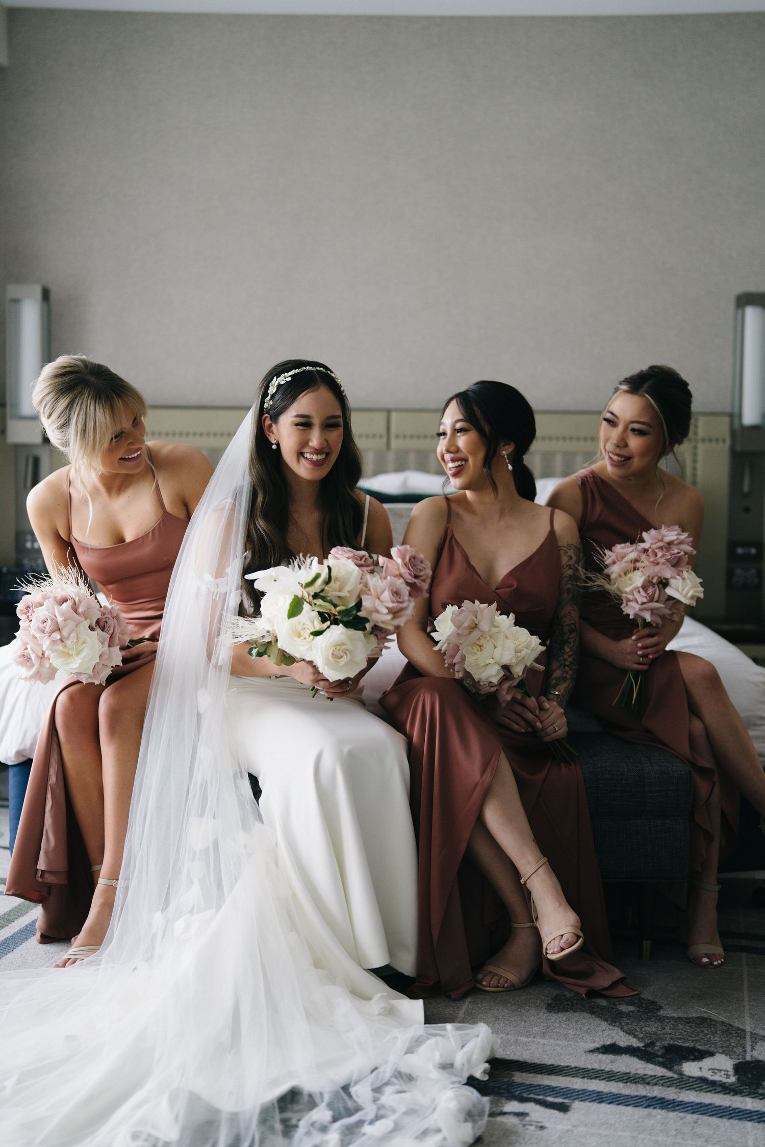Bridesmaids in mauve dresses sitting together with white and pink bouquets.