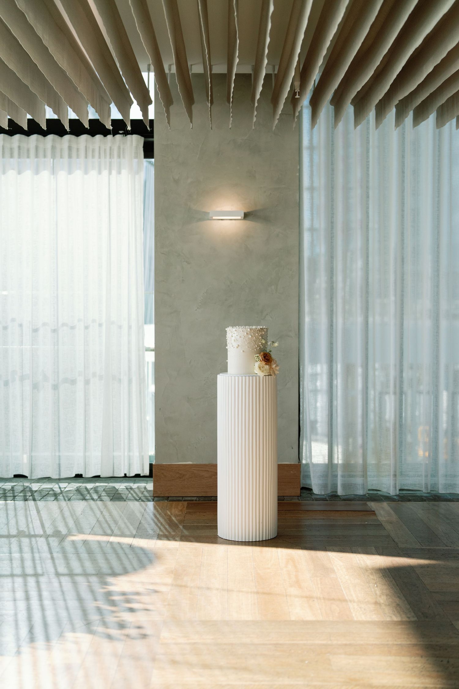 Minimalist event space with sheer curtains and sunlight casting dramatic shadows.