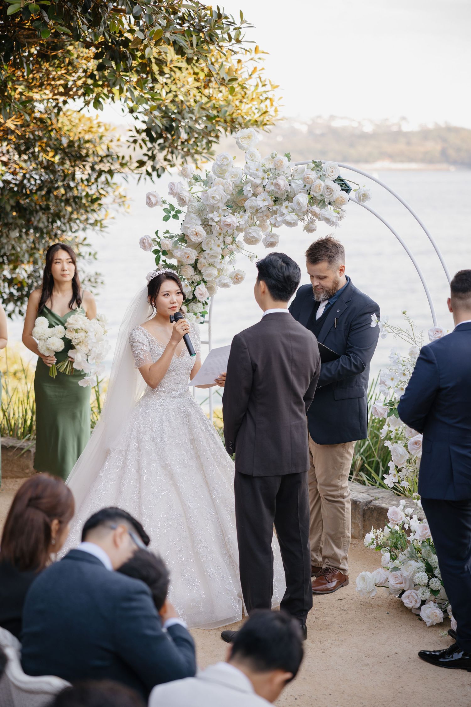 Outdoor wedding ceremony under floral arch with waterfront view.