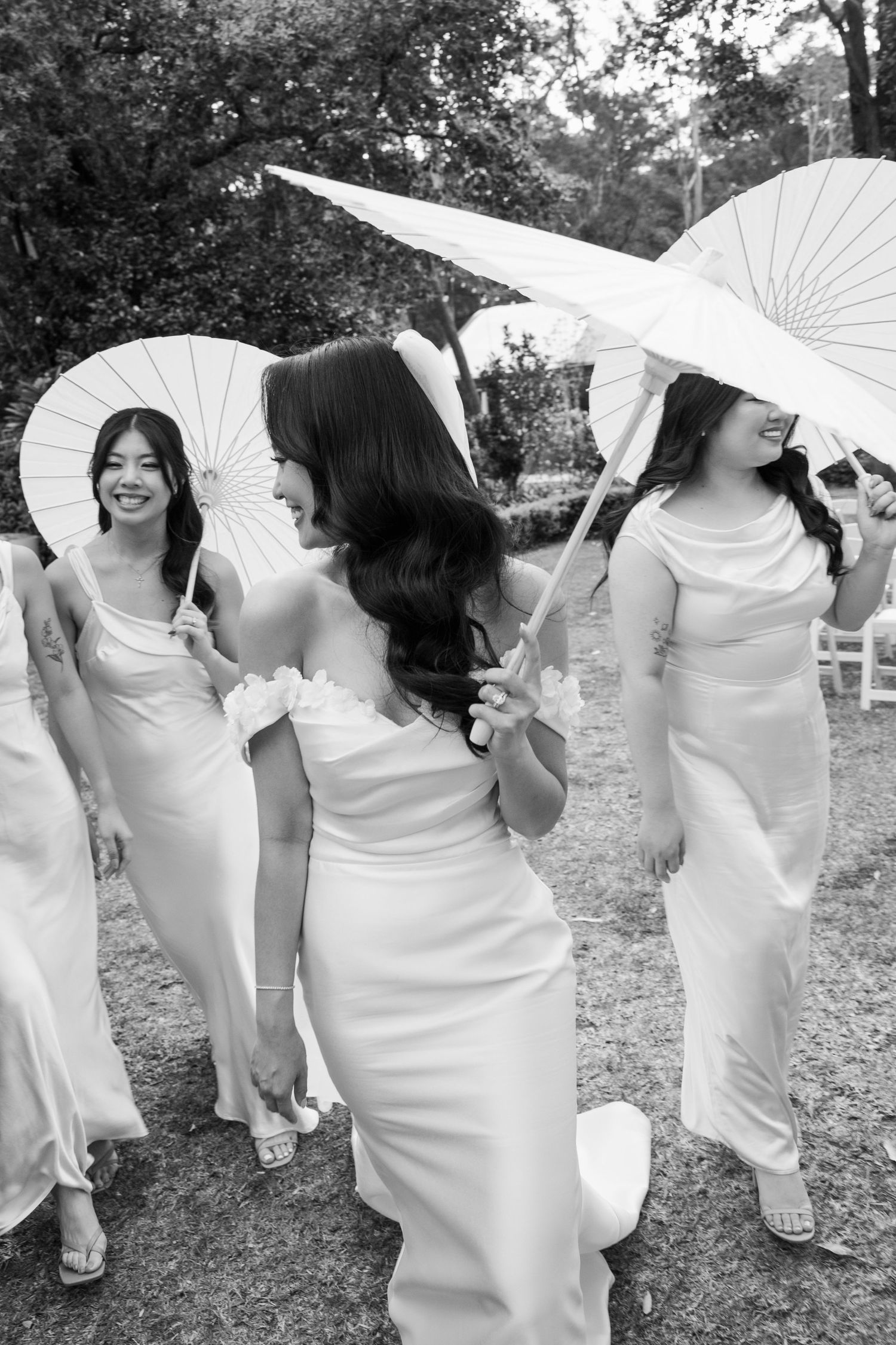 Wedding party in white dresses poses with decorative parasols in black and white.