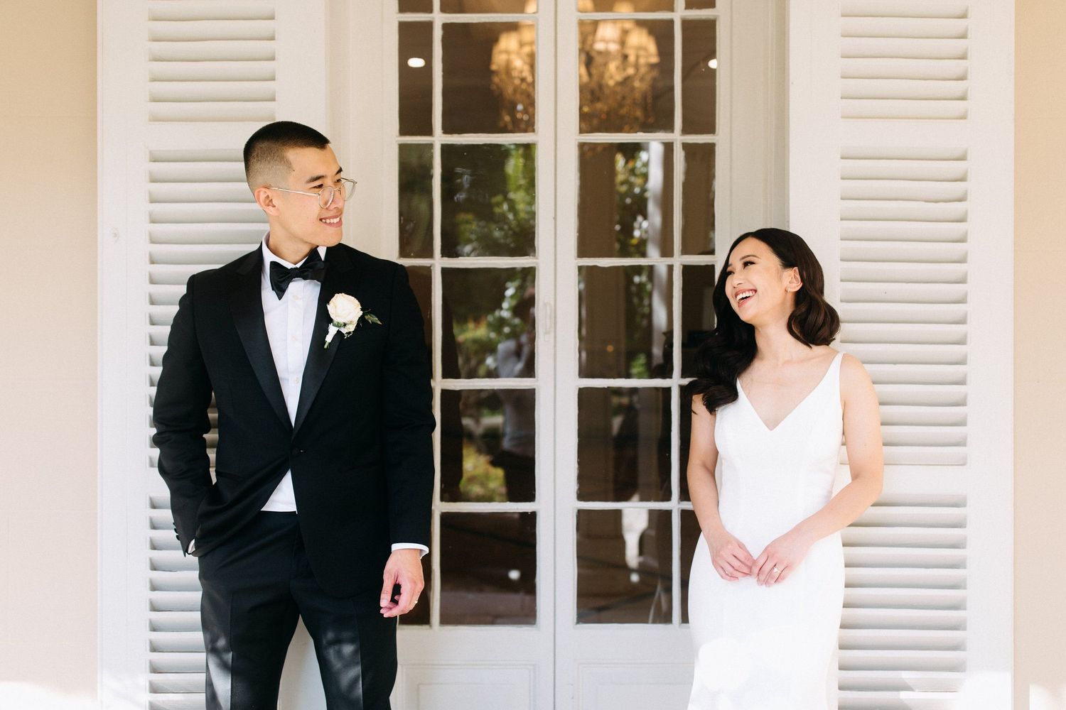 Elegant wedding couple poses in formal attire against white colonial building.